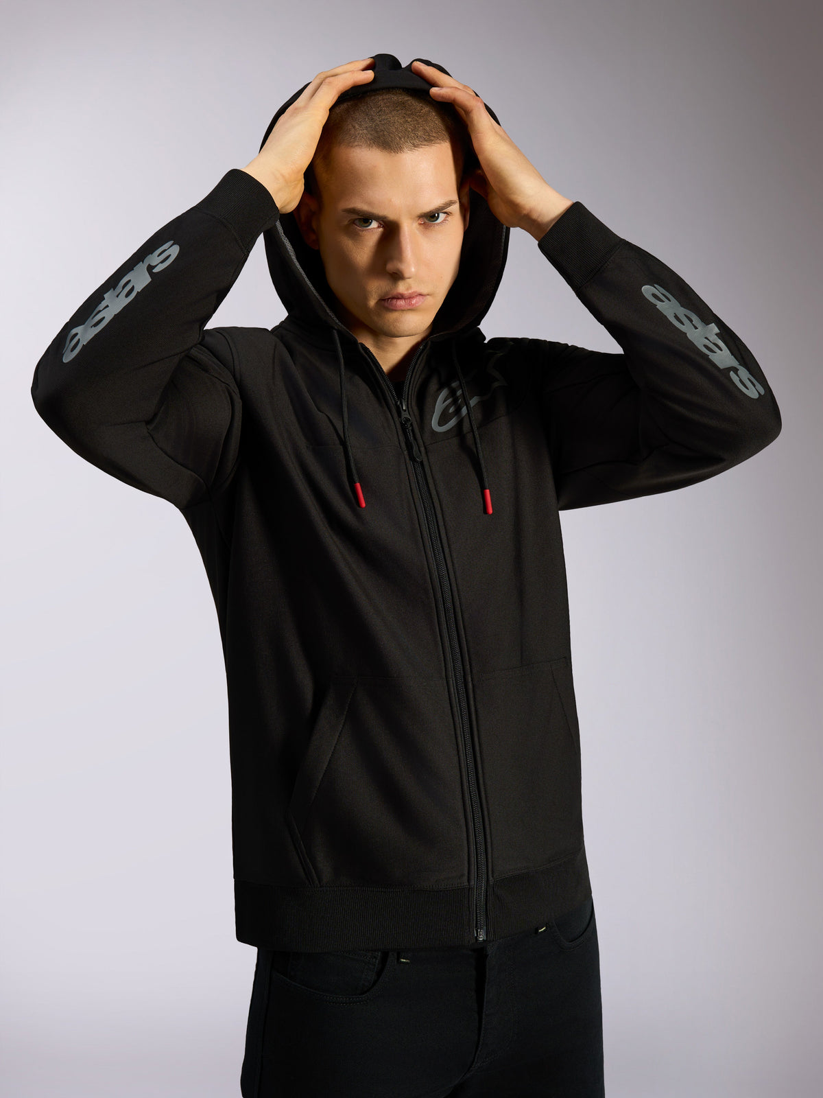 Alpinestars Sessions V3 Hoodie, hoodie preto com fecho integral, logótipo Astars cinzento nos antebraços, capuz com forro em malha e cordões com pontas vermelhas, streetwear casual inspirado no desporto motorizado