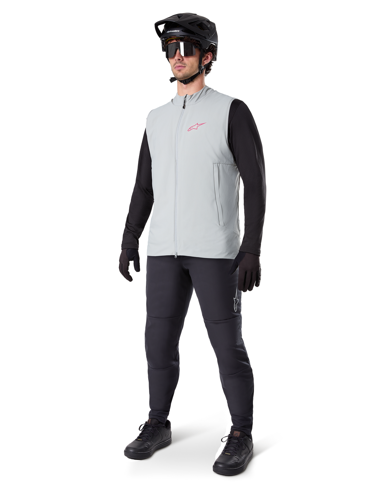 Alpinestars A-Dura Thermal Vest, Titanium gray cycling gilet with a pink logo, worn by a model with a black long-sleeve shirt, dark gray pants, and a black mountain bike helmet, performance gear for cold-weather riding