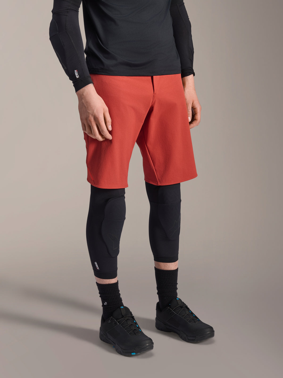 Alpinestars A-Motion Plasma Knee Sleeve, protetor de joelho para BTT, preto, usado com calções vermelhos e sapatos de BTT pretos, design slip-on de baixo perfil com proteções contornadas e malha respirável.