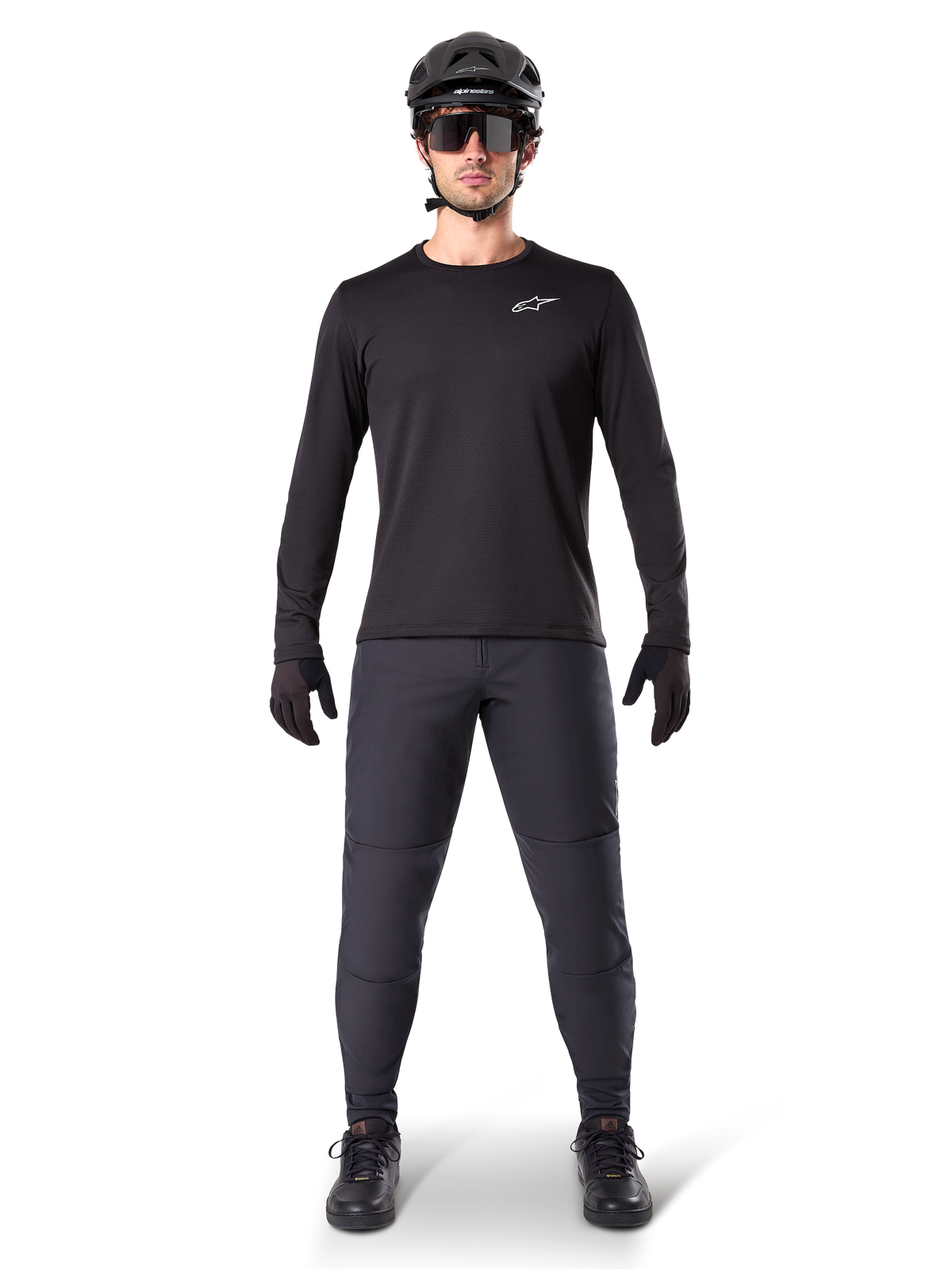Calças Térmicas Alpinestars A-Dura, pretas, usadas por um ciclista com equipamento completo de BTT, incluindo camisola preta de manga comprida, capacete e óculos de sol, calças duráveis com ajuste regular para trilhos em clima frio
