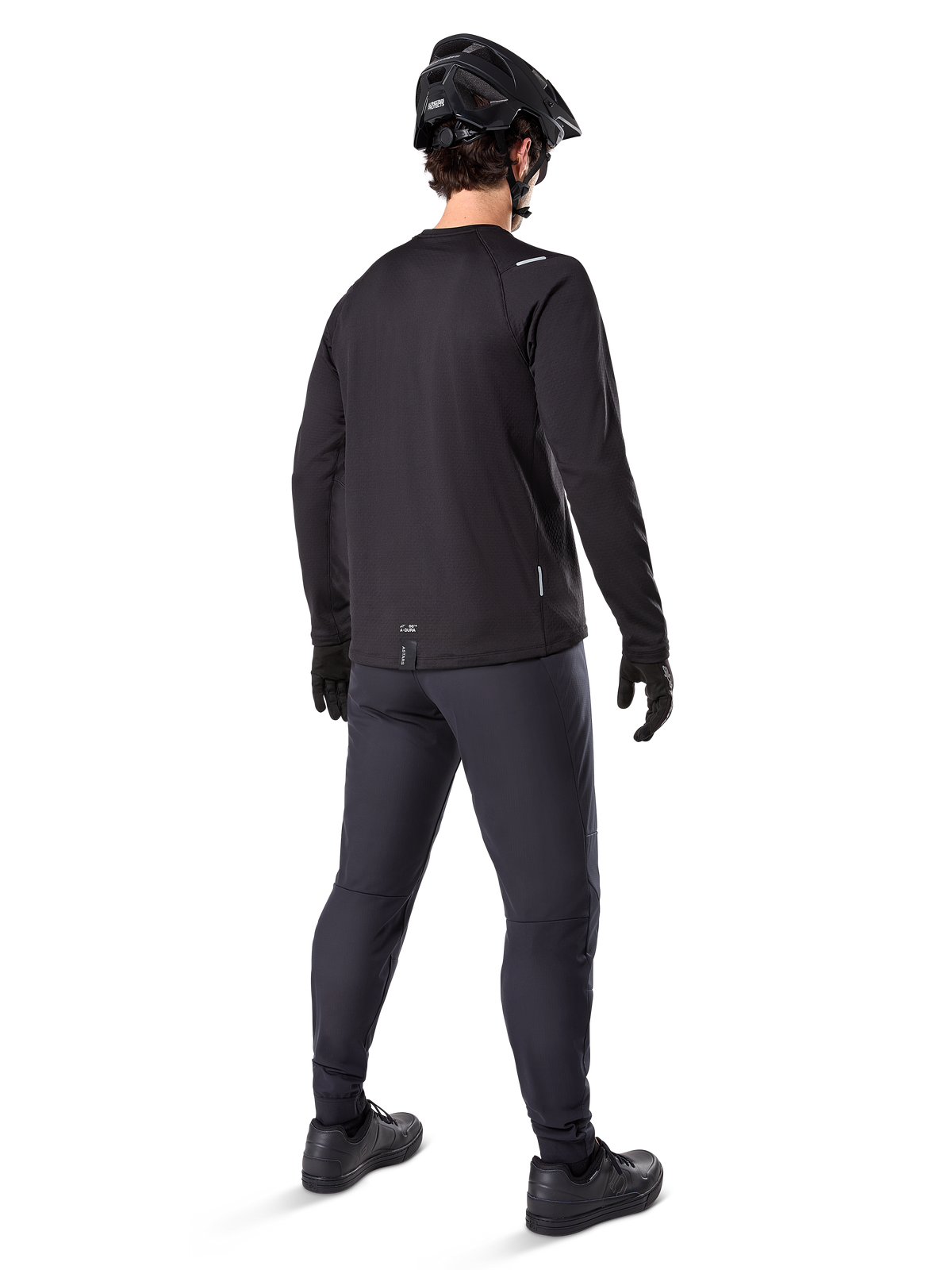 Calças Térmicas Alpinestars A-Dura, calças de BTT, pretas, vistas de uma perspetiva traseira, usadas com uma camisola de manga comprida a condizer, capacete de BTT preto e luvas, equipamento técnico de ciclismo para clima frio
