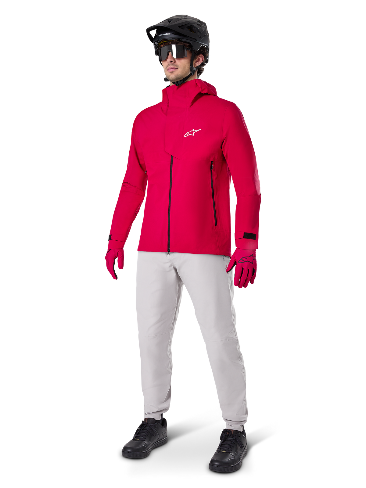 Modelo a usar Calças Impermeáveis Alpinestars A-Dura em cinzento Titanium, combinadas com um casaco impermeável vermelho vivo e luvas a condizer, capacete de BTT preto com óculos e sapatos pretos, equipamento completo de BTT para trilhos molhados