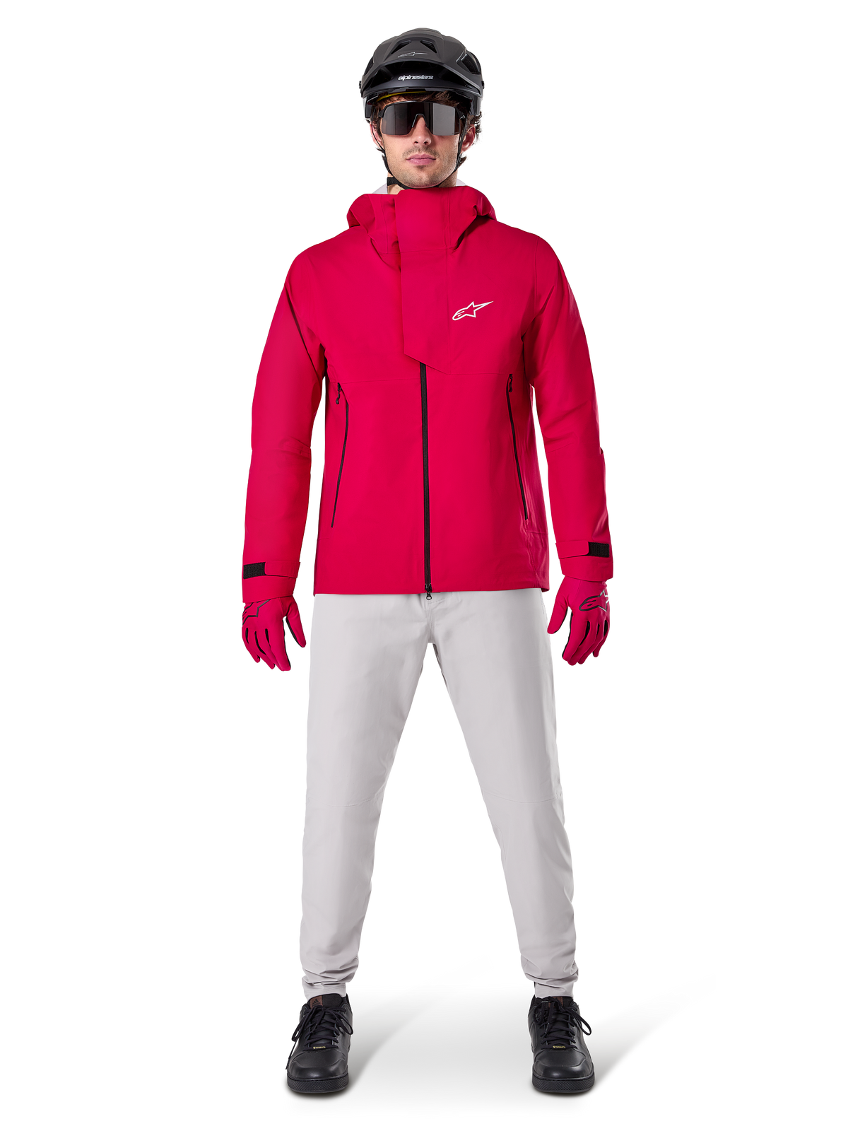 Calças Impermeáveis Alpinestars A-Dura, calças de BTT, cinzento Titanium, usadas com um casaco vermelho vivo com capuz, luvas vermelhas e um capacete de BTT preto, equipamento de ciclismo profissional impermeável para condições de trilhos molhados