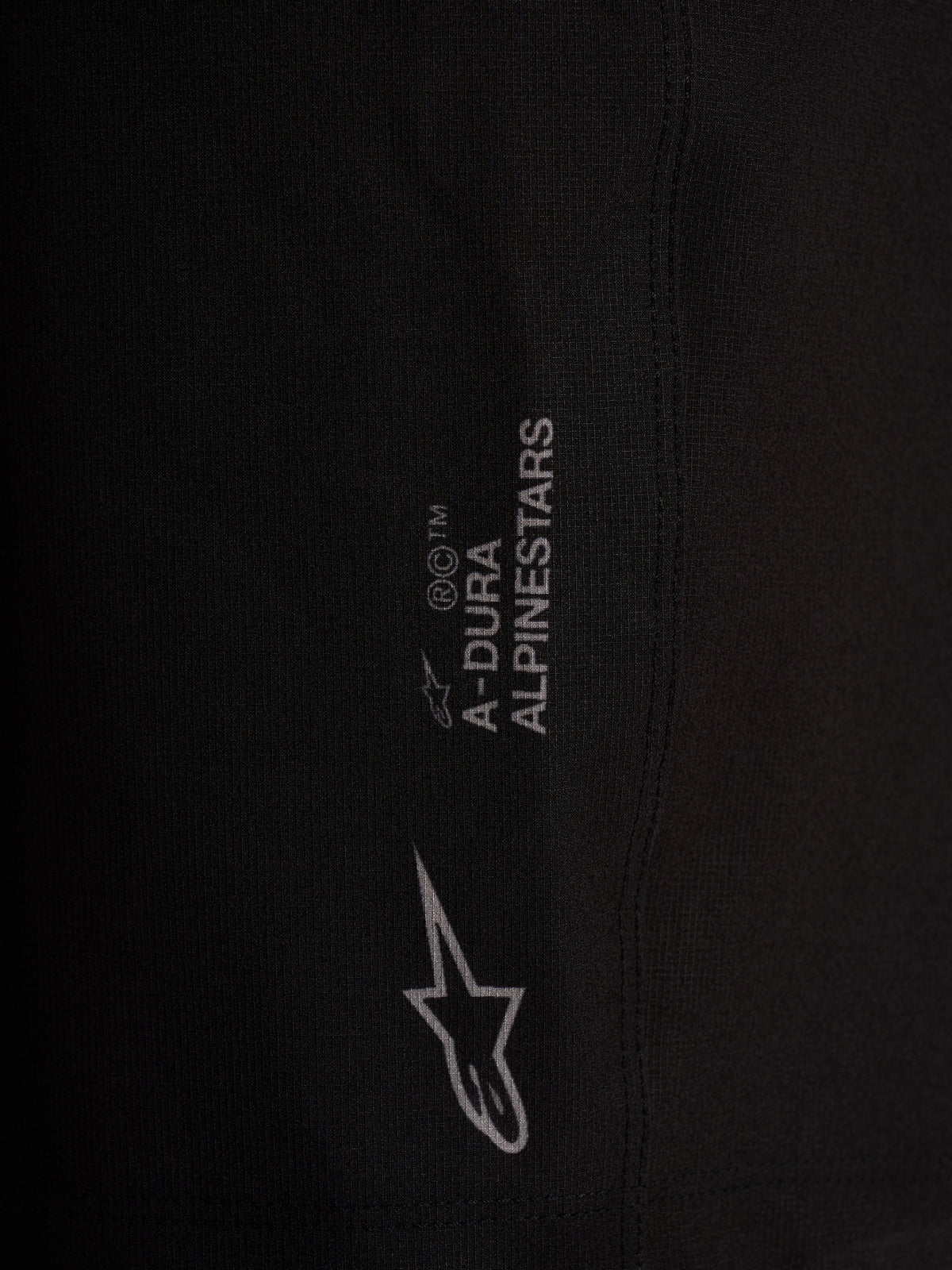 Detalhe da marca e logótipo Alpinestars nos calções pretos A-Dura Ride, em tecido elástico de alta performance.
