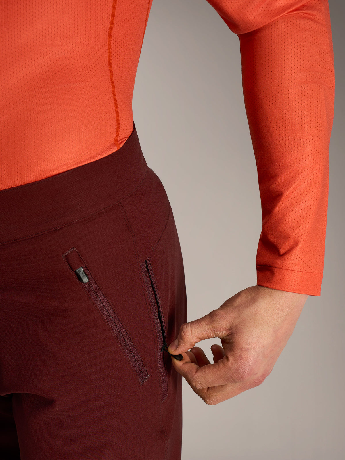 Calções Alpinestars A-Dura Ride bordeaux, pormenor de mão a abrir o bolso lateral com fecho e forro em malha.