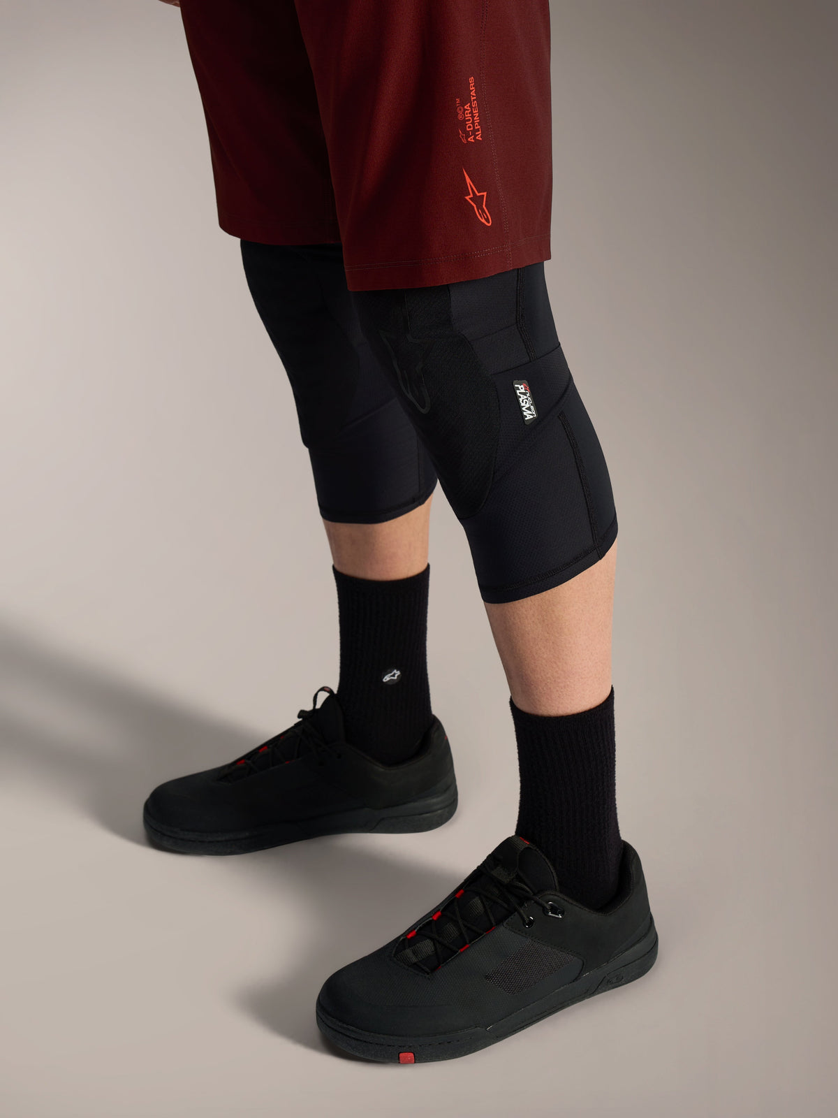 Calções Alpinestars A-Dura Ride bordeaux, elásticos e duráveis para MTB, com joelheiras e sapatos pretos.