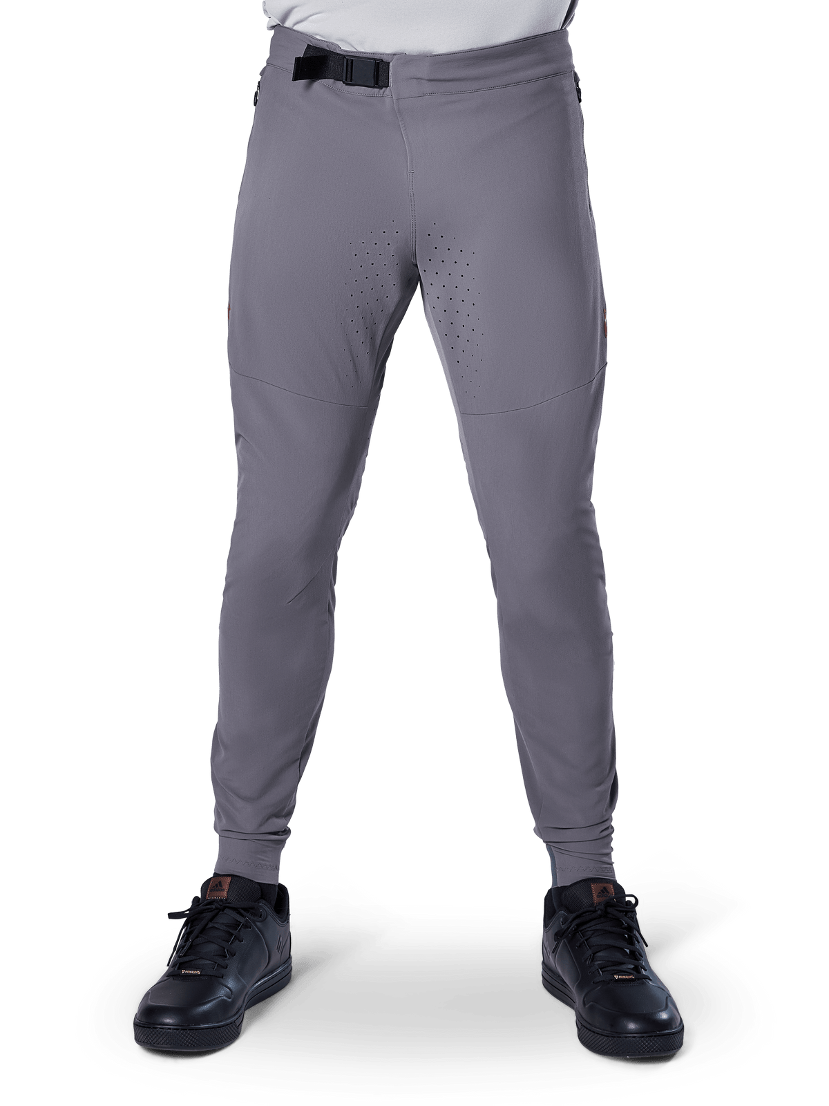 Calças Alpinestars A-Aria Elite, calças de BTT, cinzento escuro, com perfurações a laser na parte interna das coxas para ventilação e fecho de fivela magnética na cintura, corte de performance com pernas afuniladas, usadas com sapatilhas desportivas pretas