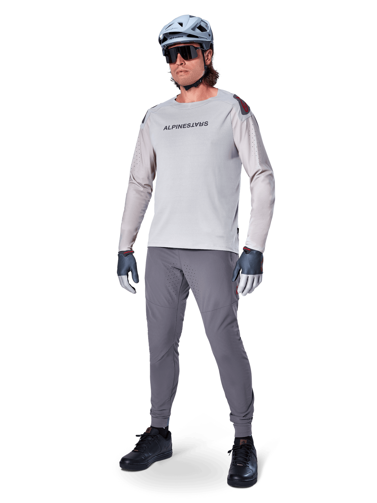 Alpinestars A-Aria Elite Pants, calças de BTT cinza escuro, vestidas por um ciclista com camisola de manga comprida cinza claro e capacete cinza, com perfurações a laser nas coxas e um ajuste de desempenho para ciclismo de montanha.
