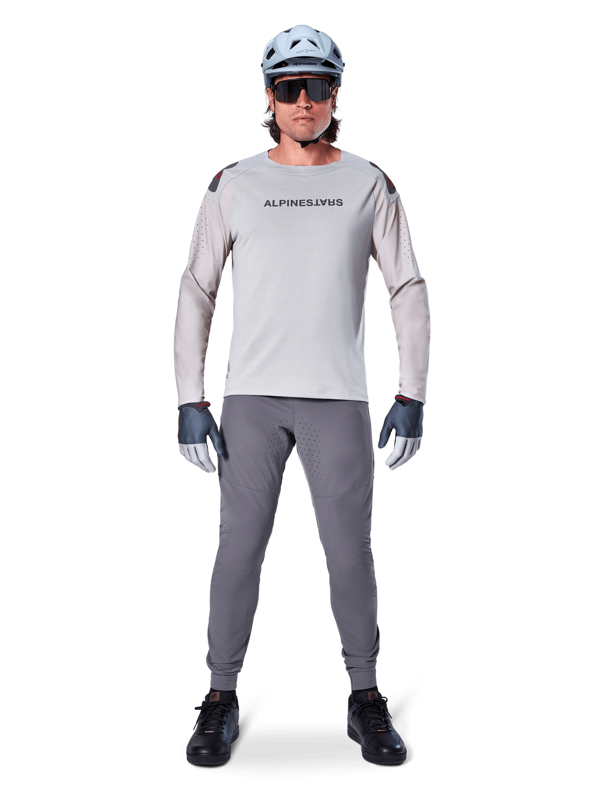 Alpinestars A-Aria Elite Pants, calças de mountain bike cinza escuro, vestidas por um ciclista com camisola de manga comprida cinza claro, capacete azul claro e sapatilhas pretas, com perfurações a laser visíveis no interior das pernas e um ajuste de performance slim.