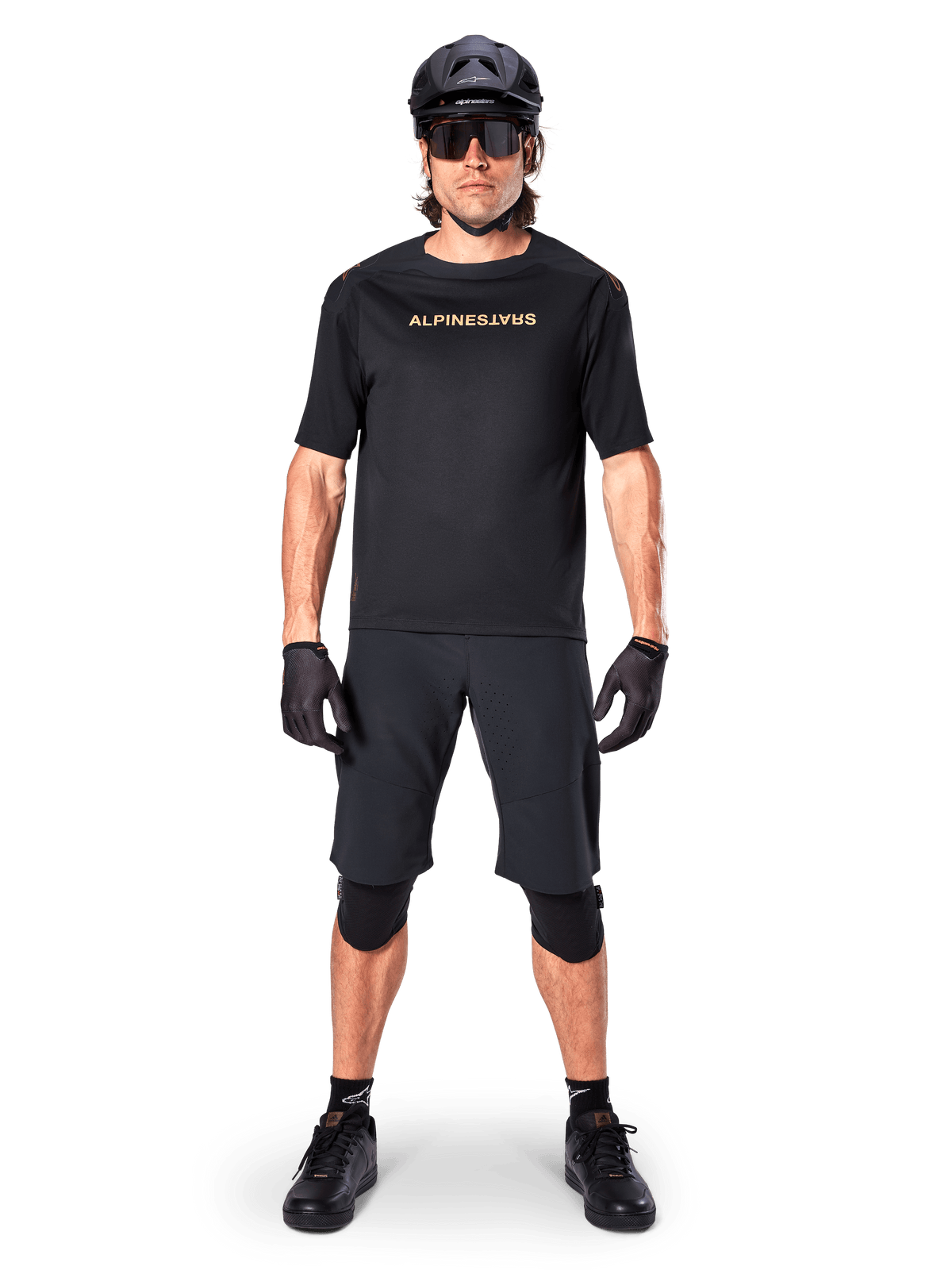 Ciclista de BTT masculino a usar os calções Alpinestars A-Aria Elite em preto, combinados com uma camisola de manga curta Alpinestars preta a condizer, capacete, luvas e joelheiras pretas, conjunto completo de equipamento de ciclismo off-road