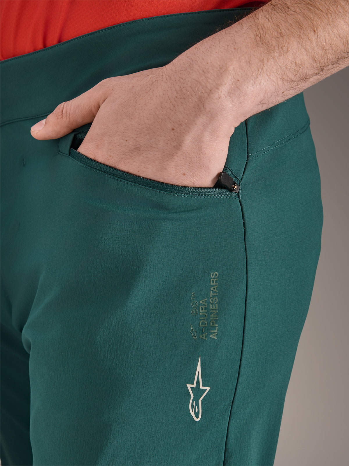Calças Alpinestars A-Dura em verde Dark Pine, grande plano do bolso com fecho de correr e mão, com o logótipo e a marca Alpinestars em branco na coxa, calças de ciclismo MTB duráveis