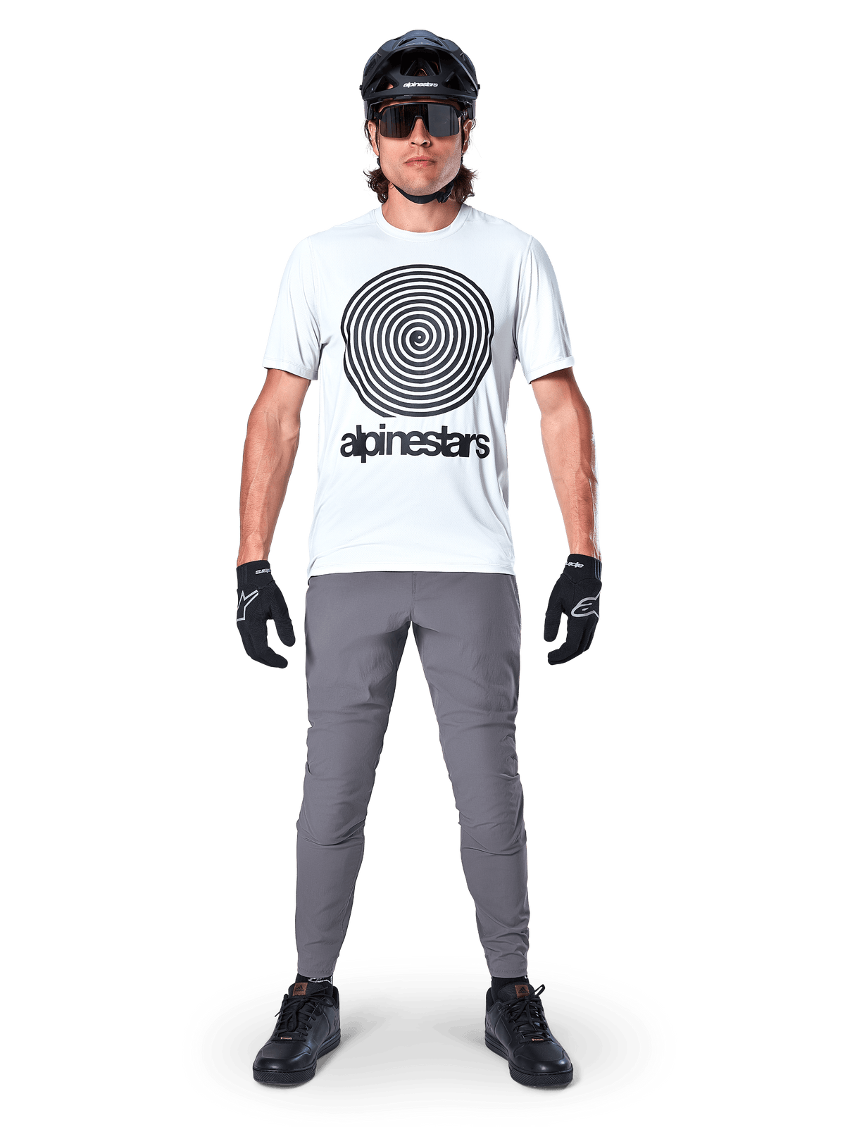Calças Alpinestars A-Dura, calças de ciclismo MTB, cinza escuro, usadas com t-shirt branca com grafismo, capacete e luvas pretos, com design durável de elasticidade bidirecional e ajuste regular para mountain bike