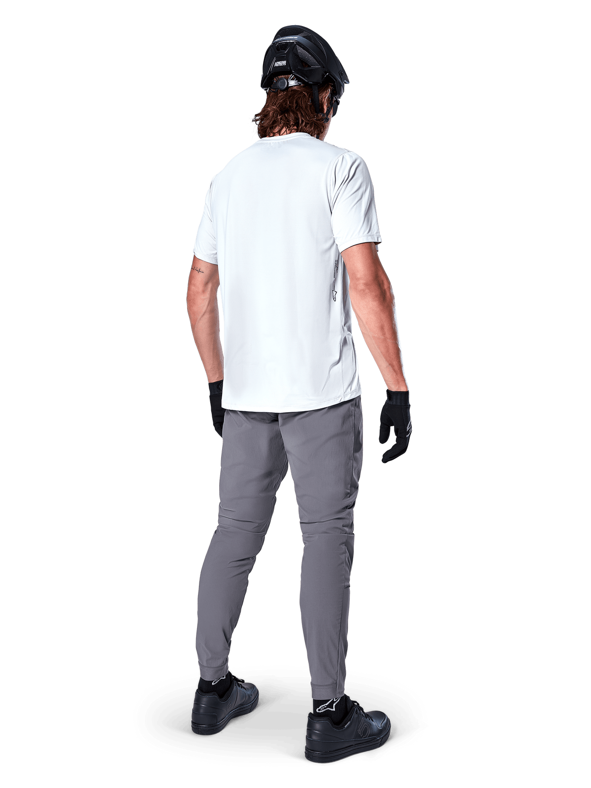 Calças Alpinestars A-Dura, calças de BTT em cinzento escuro vistas de trás, usadas com uma t-shirt branca de manga curta, capacete de BTT preto, luvas e sapatos pretos, design de corte regular com punhos elásticos, equipamento de ciclismo todo-o-terreno durável