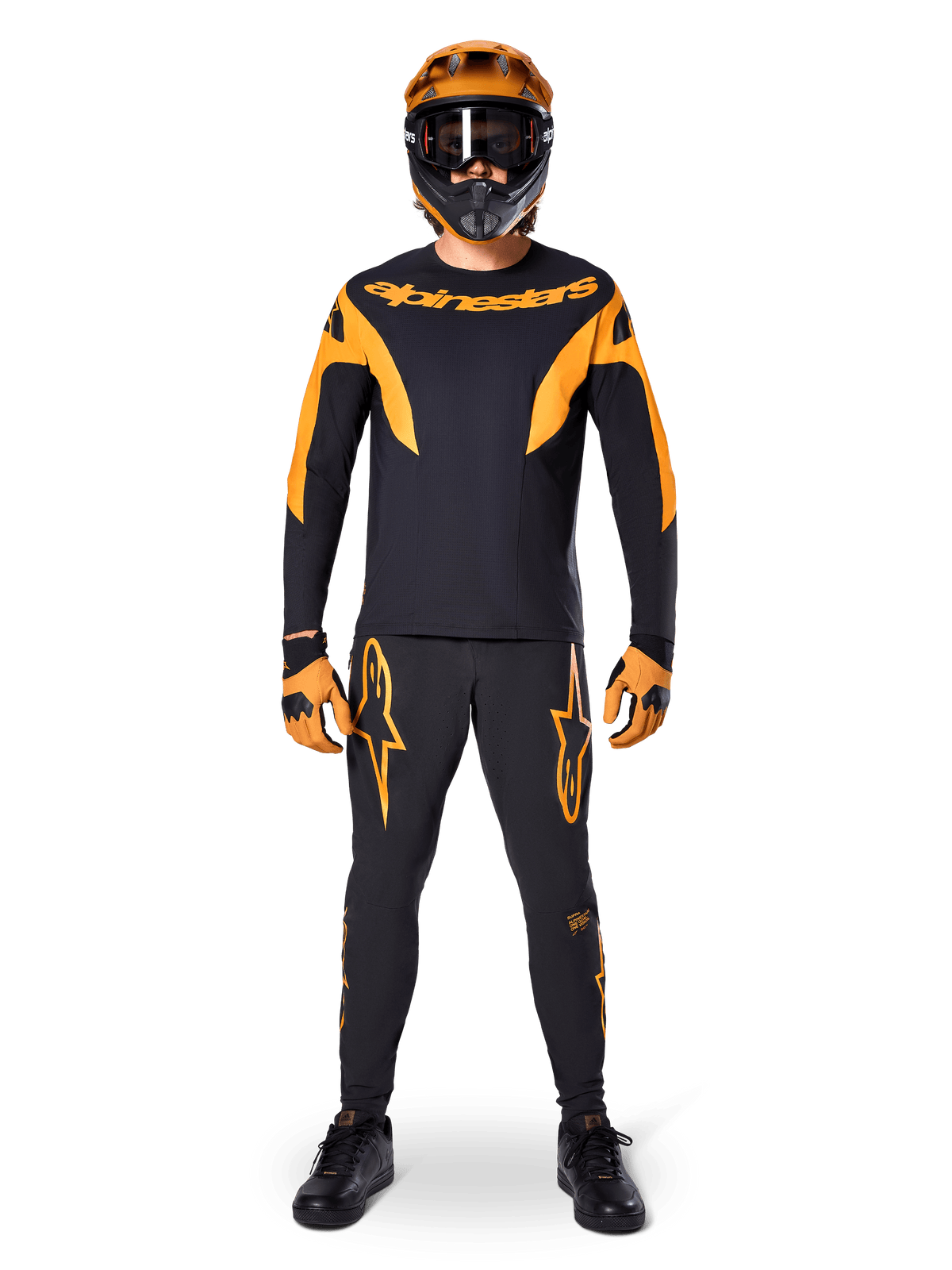 Calças Alpinestars A-Supra Race, calças de corrida de MTB, pretas e laranja, vestidas por um piloto num kit completo com camisola preta e laranja, capacete laranja e luvas a condizer, com logótipos de estrela laranja destacados nas pernas