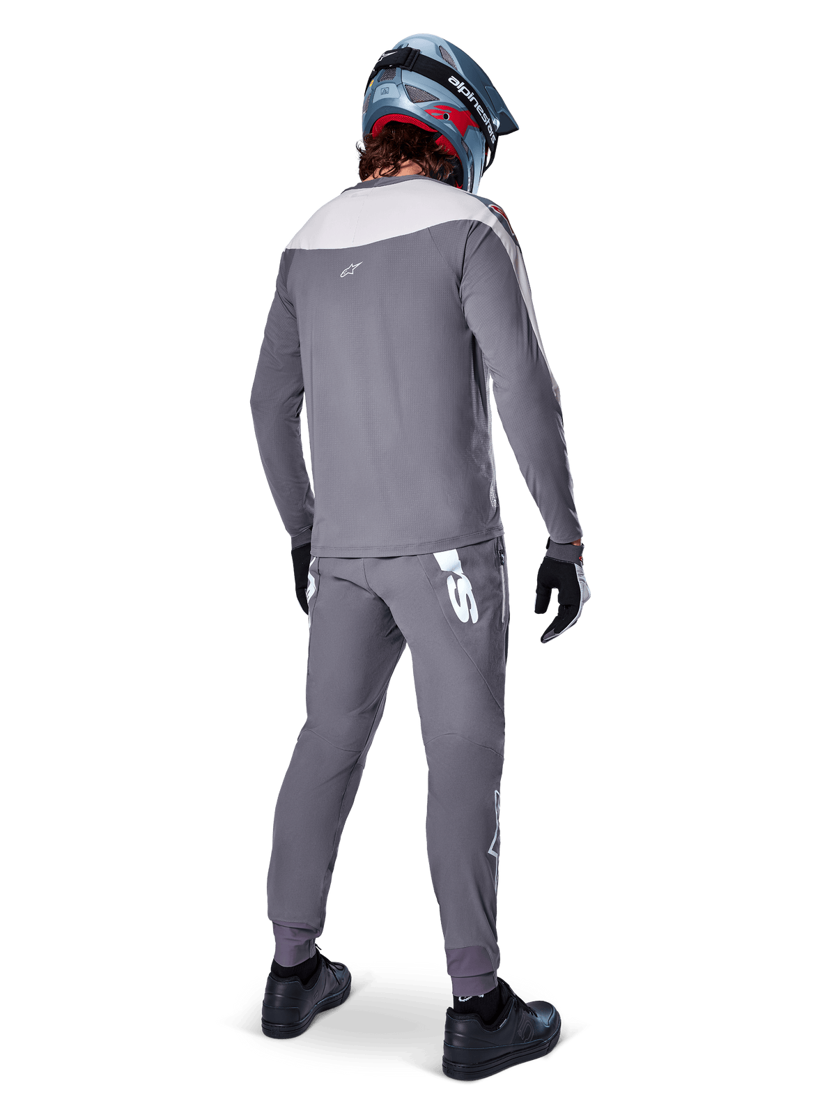 Alpinestars Calças A-Supra Race, cinza escuro, ciclista de BTT visto de costas com equipamento completo de corrida, camisola cinzenta de manga comprida, calças cinza escuro com logótipo branco de inspiração MX na pala traseira, capacete cinzento e azul, sapatos pretos, concebidas para performance em BTT
