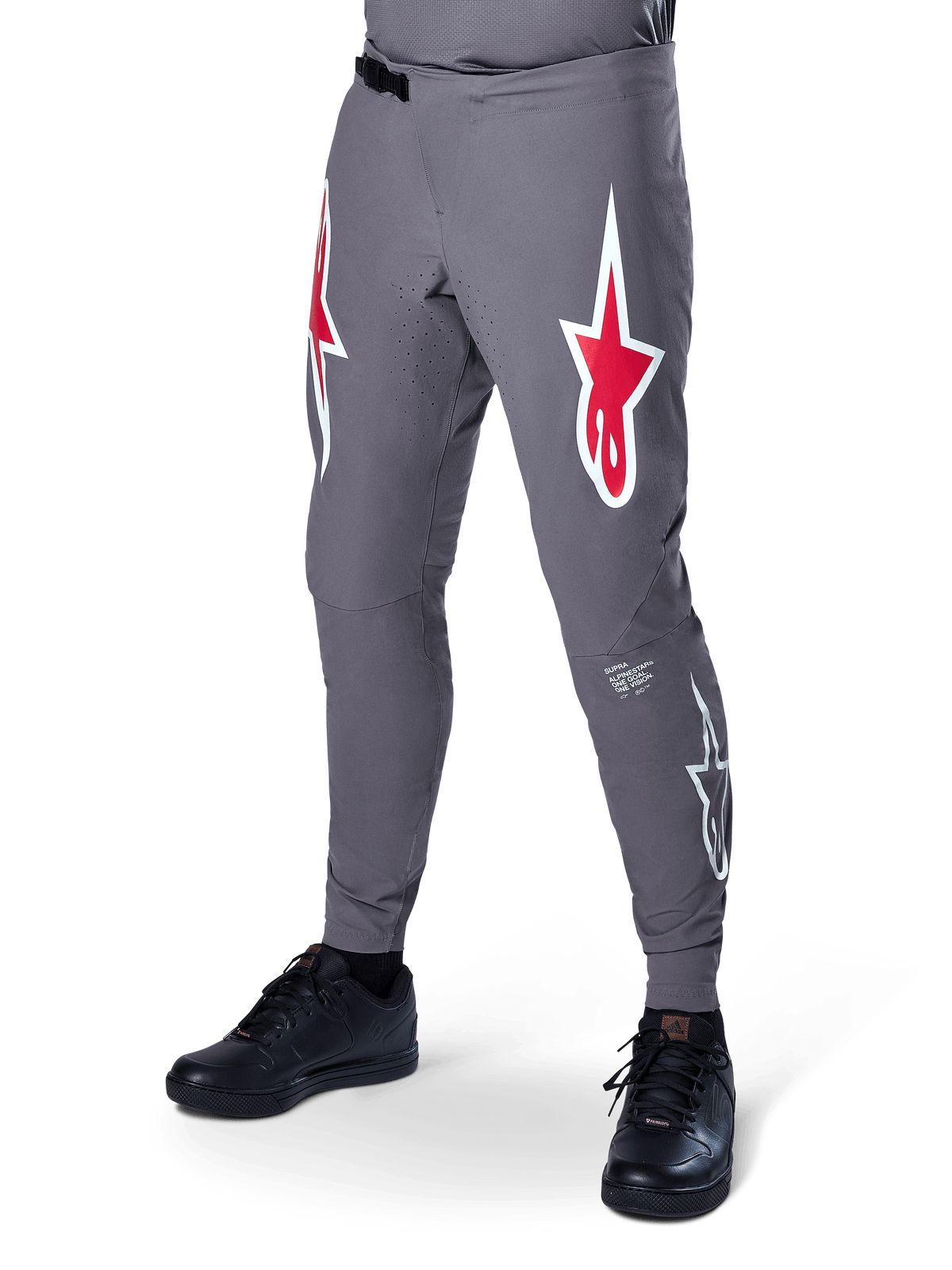 Alpinestars A-Supra Race Pants, calças de ciclismo de montanha em cinza escuro, com grandes logótipos de estrela vermelhos e brancos nas coxas, perfurações a laser para ventilação e fecho de cintura por catraca, ajuste de performance para downhill e enduro