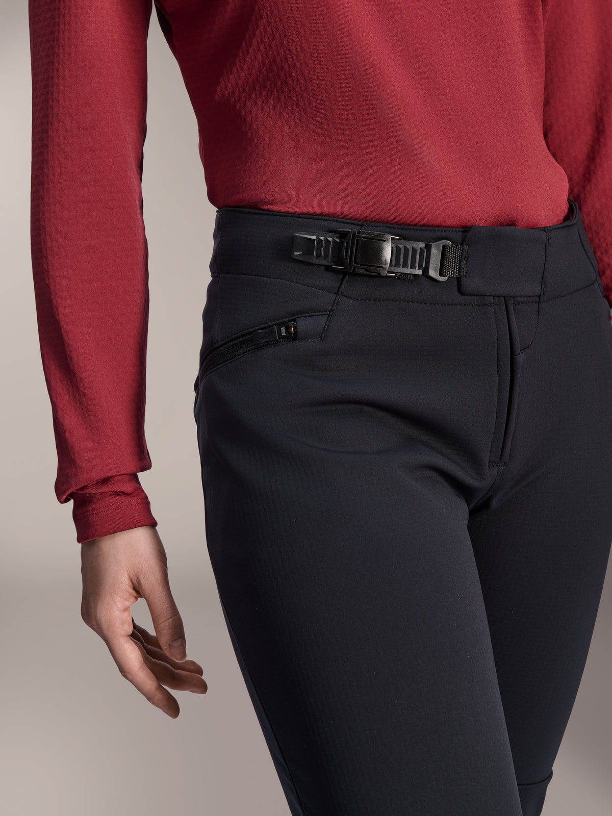 Calças Térmicas Alpinestars Stella A-Dura, calças de BTT para mulher, pretas, plano de pormenor que mostra o sistema de fecho de catraca na cintura e o bolso lateral com fecho de correr, usadas com uma camisola de manga comprida vermelho escuro, equipamento durável para trilhos em clima frio