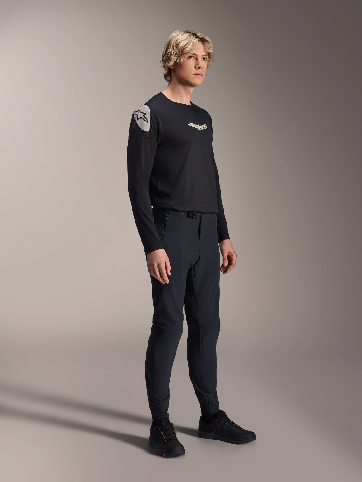 Modelo a usar camisola de manga comprida Alpinestars A-Aria Polartec Elite em preto, combinada com calças técnicas de mountain bike pretas e sapatos pretos, vestuário de ciclismo de alta performance para todo-o-terreno, fotografia de estúdio.