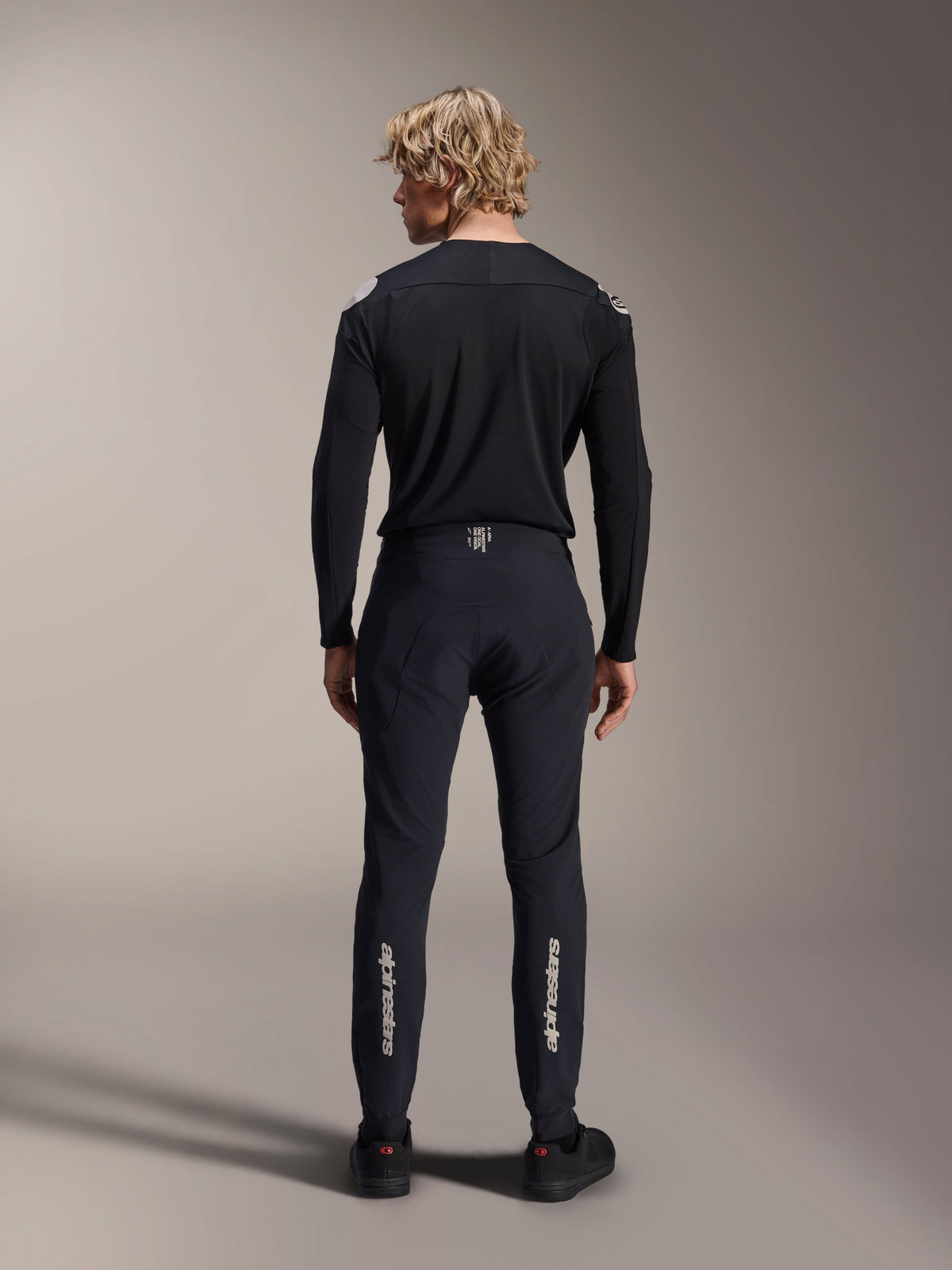 Alpinestars A-Aria Polartec Elite Long Sleeve Jersey, camisola de BTT preta, vista traseira, usada com calças pretas a condizer, ajuste de desempenho para mountain bike, com tecido técnico de absorção de humidade e branding subtil na parte inferior das costas