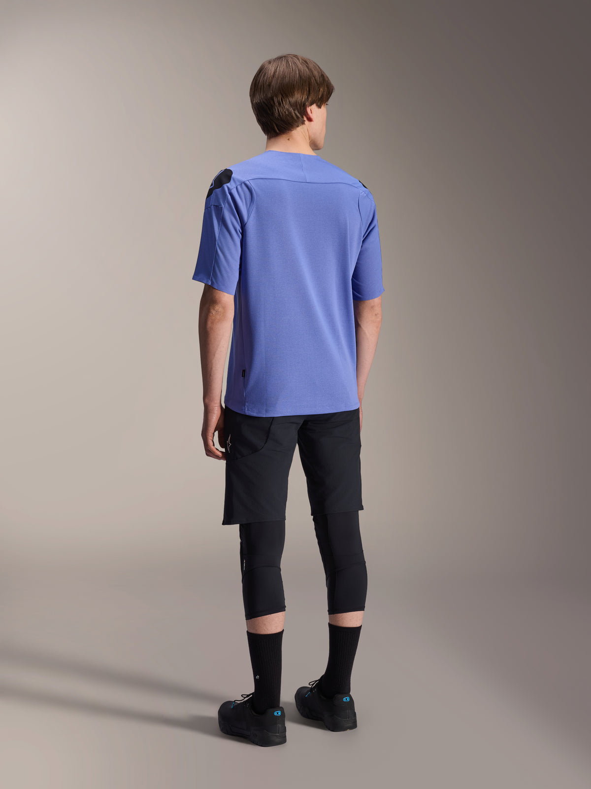 Alpinestars A-Aria Lite Short, calções de BTT pretos, combinados com uma camisola de manga curta azul A-Aria Polartec Elite e joelheiras pretas, vista traseira de um ciclista com equipamento de performance para trilhos fora de estrada.