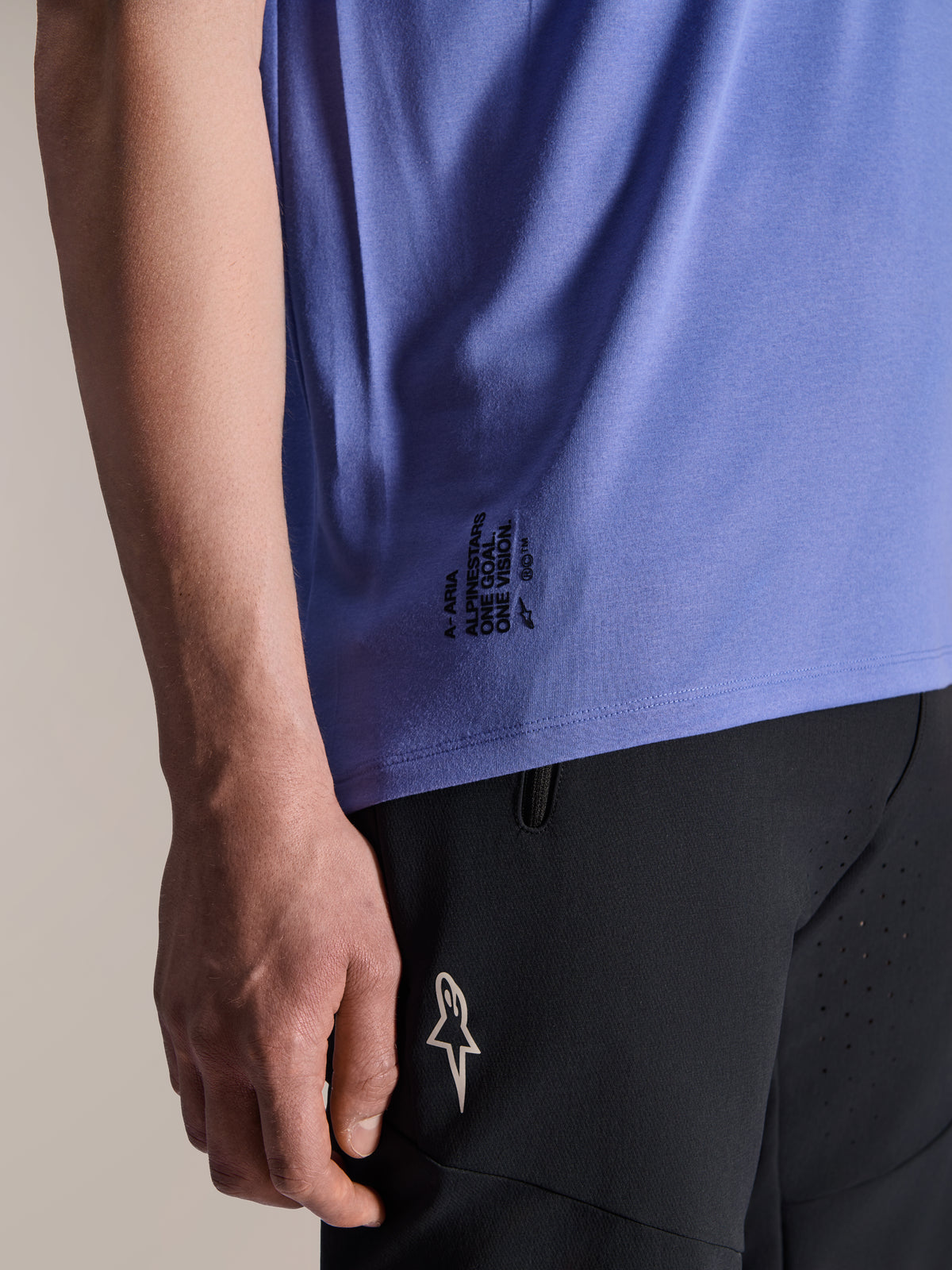 Camisola de manga curta Alpinestars A-Aria Polartec Elite em Baja Blue, detalhe da bainha lateral inferior com o texto preto 'One Goal. One Vision.' e o logótipo ASTARS, combinada com calções pretos de mountain bike.