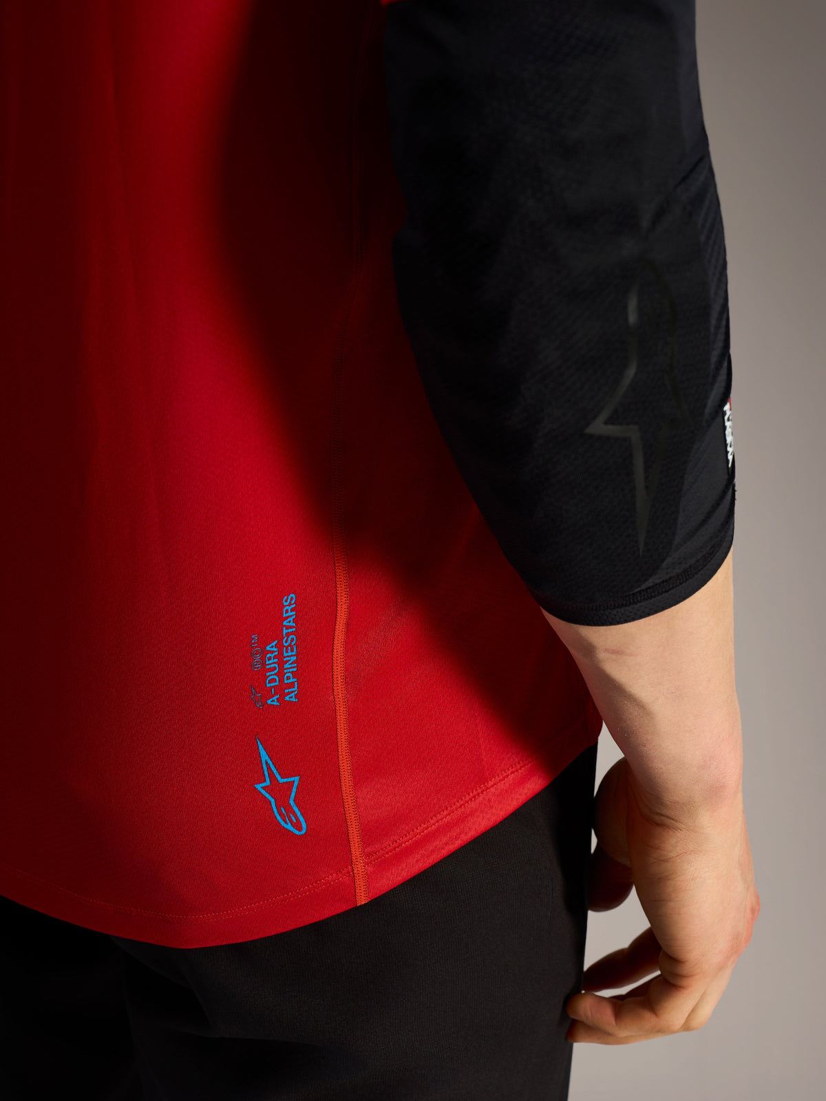 Camisola A-Dura Ride vermelha, detalhe dos logótipos Alpinestars azuis e tecido técnico de performance para BTT.