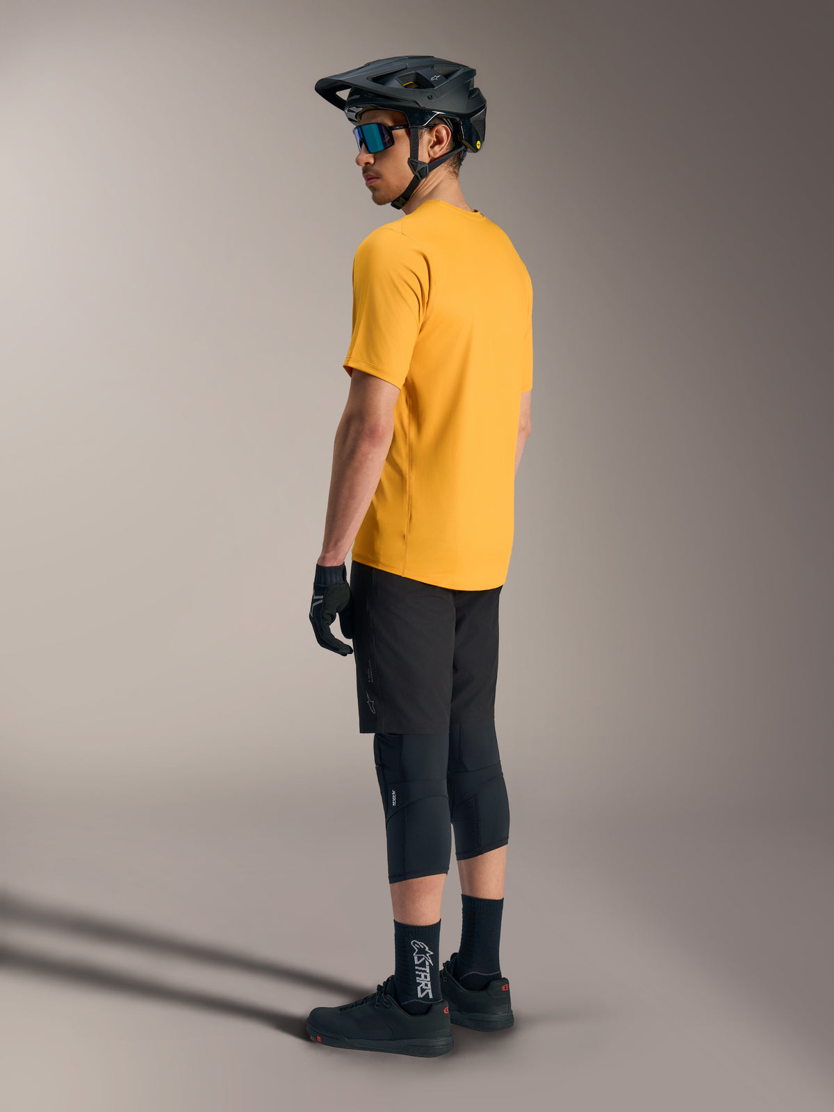 Camisola Alpinestars A-Dura Ride laranja, manga curta, vista de costas num ciclista com equipamento de BTT preto.