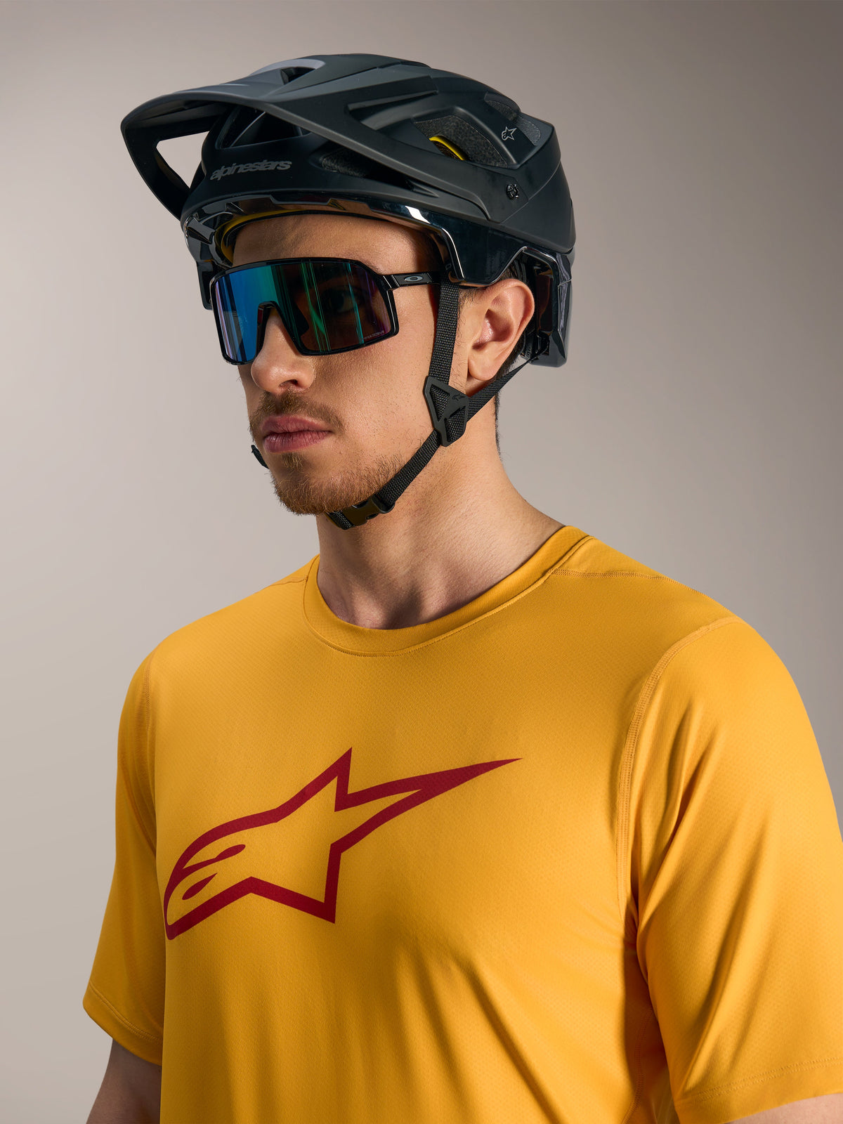 Camisola A-Dura Ride de mangas curtas laranja com logótipo Astars vermelho, capacete de BTT preto e óculos desportivos.