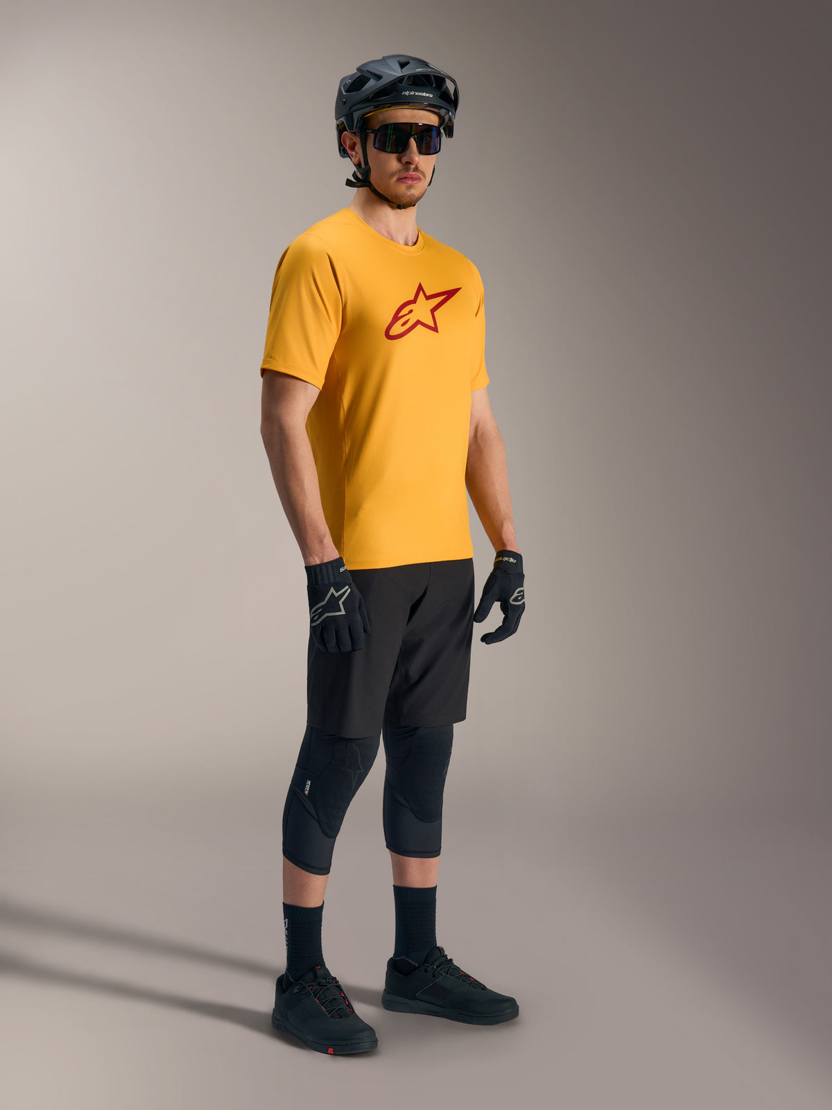 Camisola A-Dura Ride de mangas curtas laranja com logótipo Astars vermelho, equipamento de BTT preto e capacete.