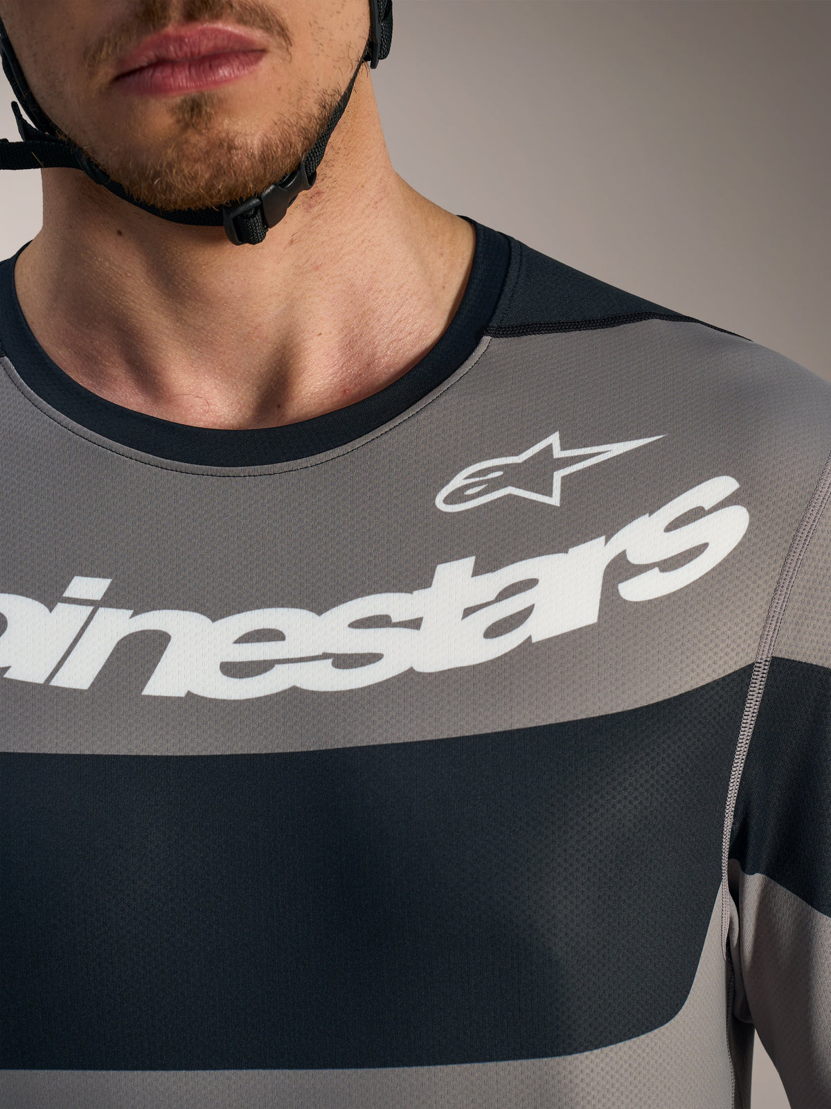 Camisola Alpinestars A-Dura Race cinzenta, detalhe do peito com logótipos brancos e malha técnica respirável.