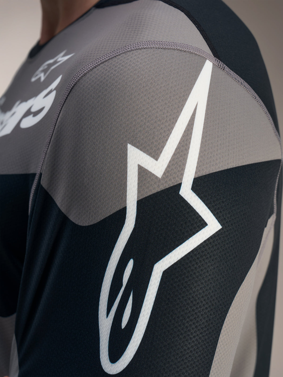 Camisola Alpinestars A-Dura Race cinzenta, detalhe do logótipo Astars branco em malha jacquard técnica texturizada.