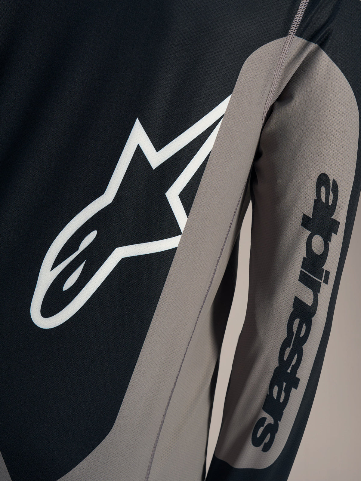 Detalhe da camisola A-Dura Race cinzenta com logótipo Astars branco e marca Alpinestars na manga comprida.