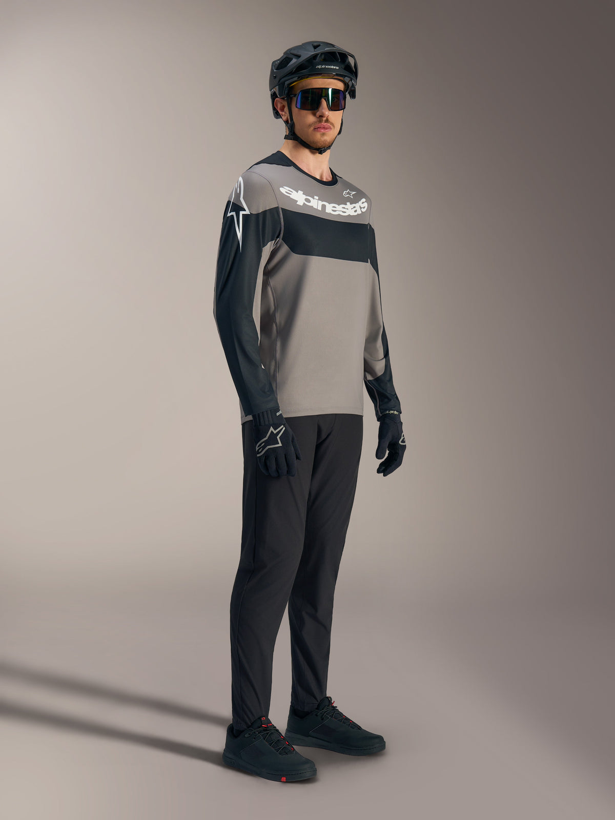 Camisola A-Dura Race de manga comprida, cinzenta e preta com logótipos brancos, calças de BTT de performance e capacete.