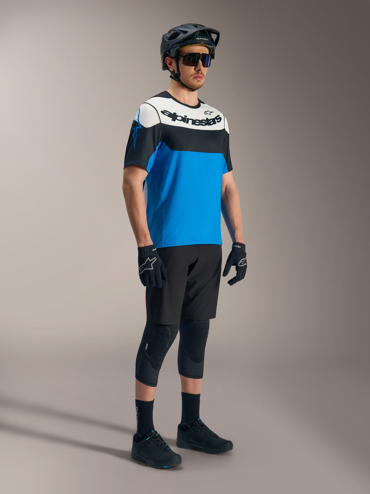 Camisola Alpinestars A-Dura Race SS em azul, preto e branco, calções A-Dura Ride e equipamento de proteção BTT.
