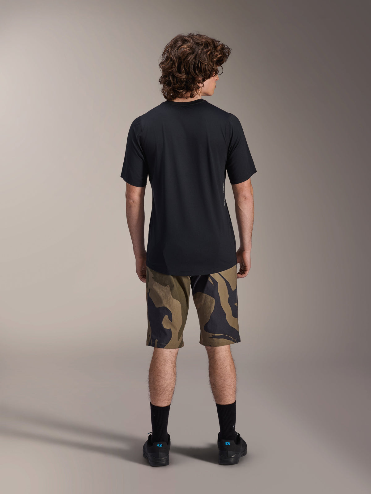 Camisola de Manga Curta Alpinestars A-Dura Astar, preta, vista traseira num modelo combinada com calções de BTT com padrão camuflado e calçado preto, vestuário técnico casual de mountain bike