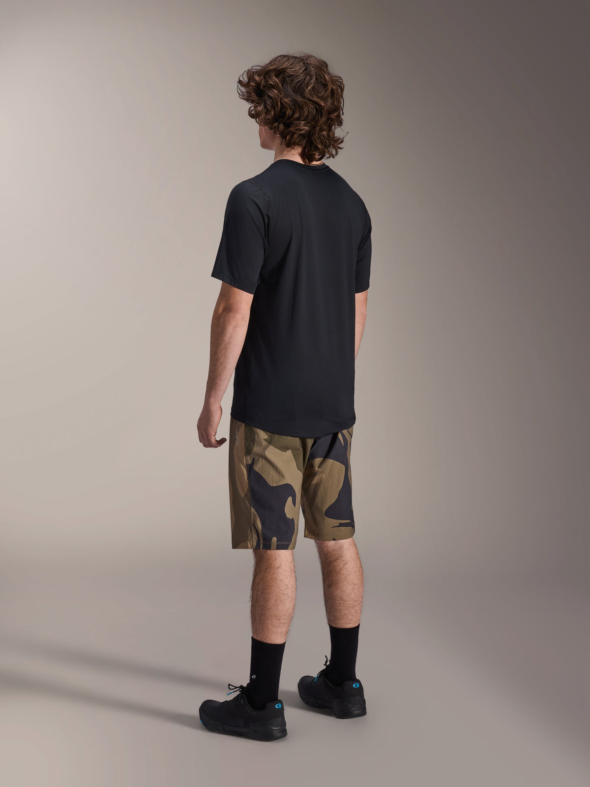 Camisola de Manga Curta Alpinestars A-Dura Astar em preto, vista de trás, combinada com calções de padrão camuflado, meias e sapatos desportivos pretos, equipamento casual de BTT