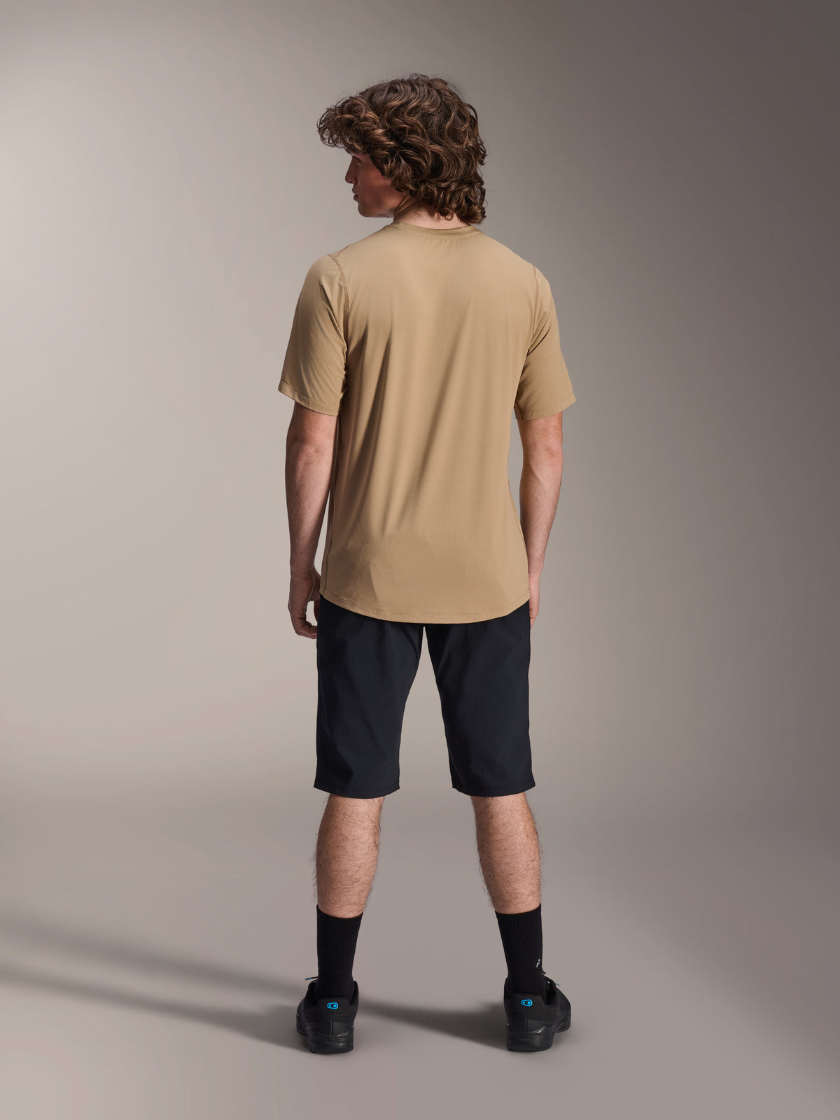 Male model from behind wearing Alpinestars A-Dura Liner Shorts in Black and a tan short-sleeve jersey, paired with black socks and shoes, durable mountain bike apparel for off-road cycling.