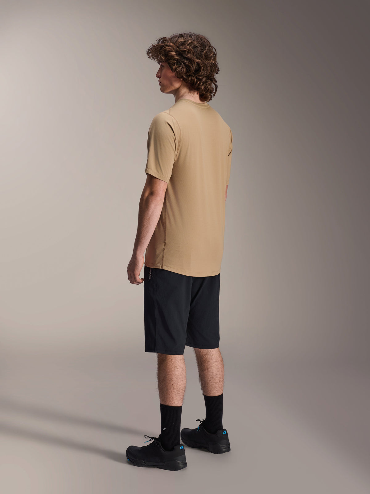 Camisola de Manga Curta Alpinestars A-Dura Astar, Castanho Claro, usada com calções pretos e meias pretas, tecido jacquard que absorve a humidade, vestuário de performance casual para mountain bike