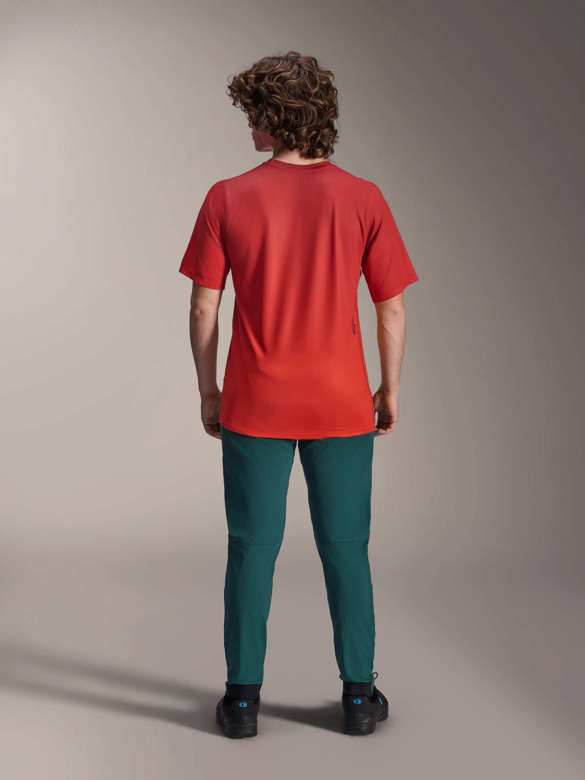 Calças Alpinestars A-Dura em verde Dark Pine, calças de mountain bike combinadas com uma camisola vermelha de manga curta, vista traseira, ajuste atlético para ciclismo fora de estrada