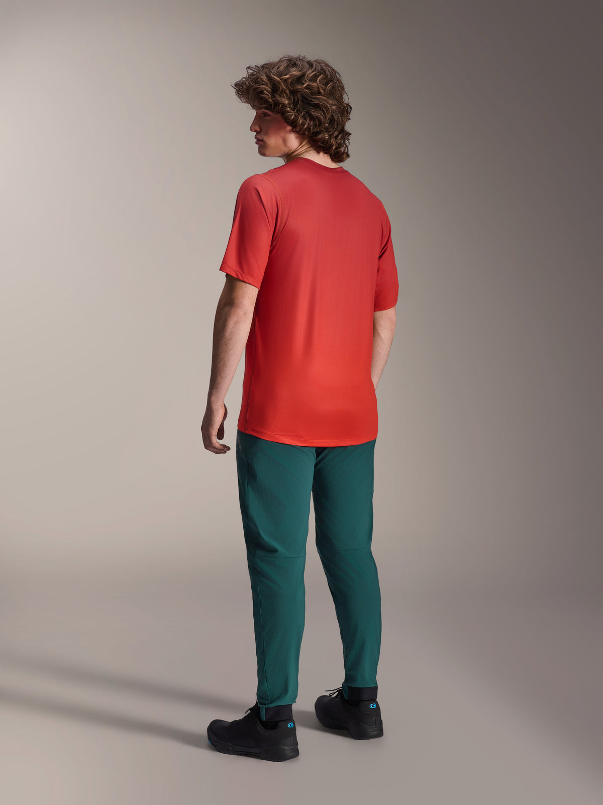 Modelo visto de costas a usar calças Alpinestars A-Dura em verde Dark Pine e uma camisola de manga curta A-Dura Rise vermelha, com corte regular e punhos elásticos, vestuário de performance para BTT e condução fora de estrada