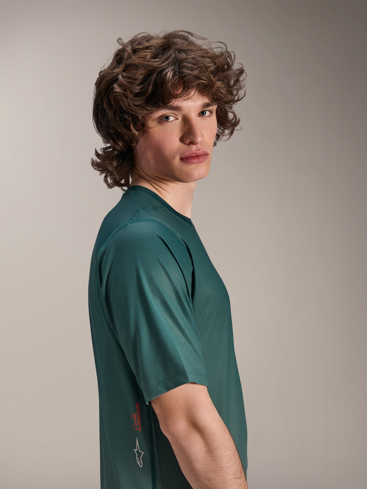 Camisola Alpinestars A-Dura Rise, camisola de BTT de manga curta, verde Silver Pine, modelo masculino a vestir tecido jacquard com absorção de humidade, logótipo A-Dura Alpinestars vermelho e logótipo branco na lateral, equipamento de trail de alta performance