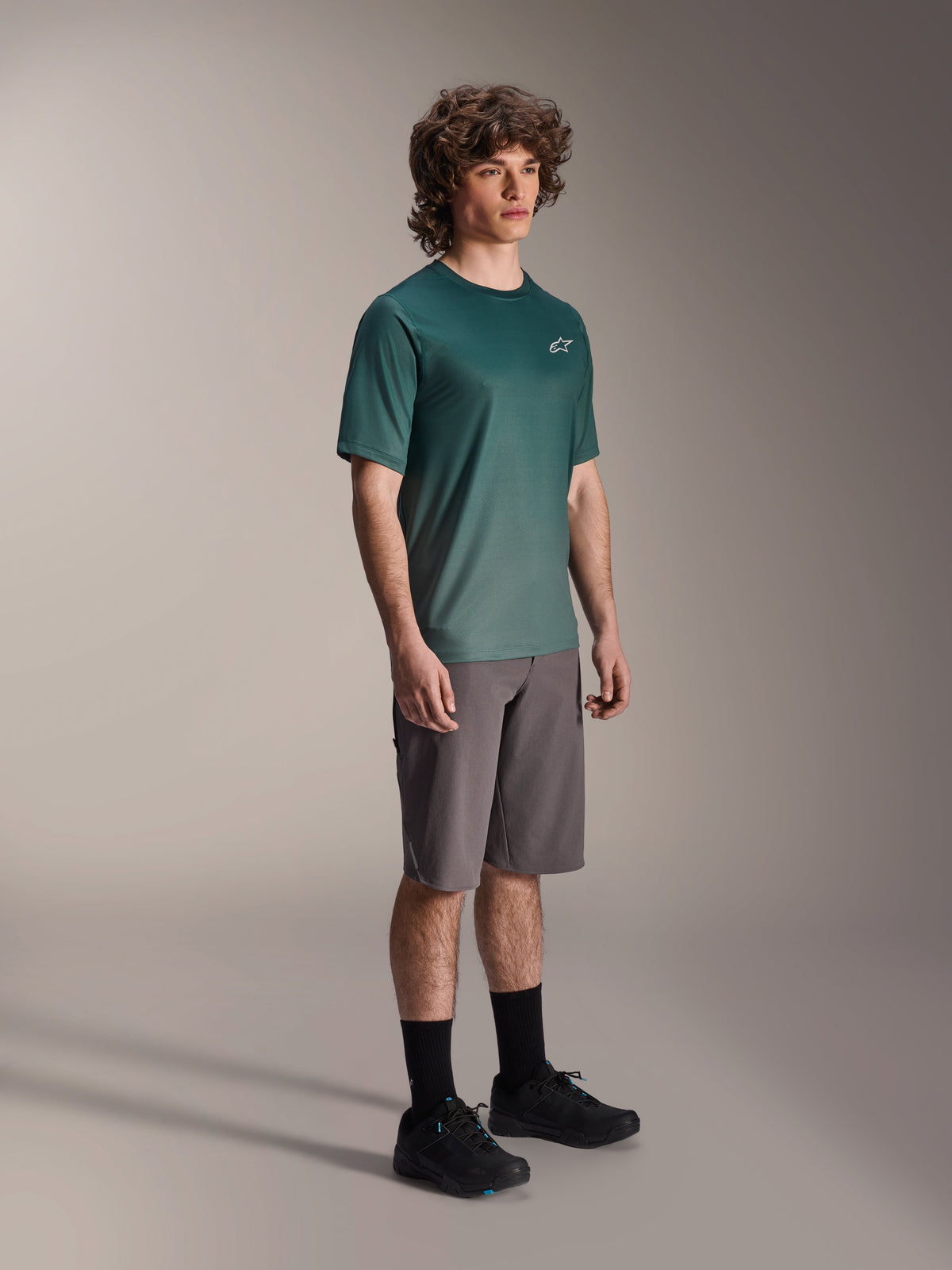 Alpinestars A-Dura Rise Jersey - Manga Curta em Silver Pine, camisola de BTT verde vestida por um modelo com calções cinzentos e sapatilhas pretas, equipamento casual para trilhos de BTT com um pequeno logótipo branco no peito