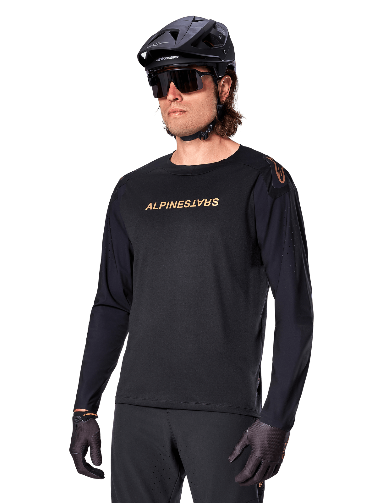 Jersey de manga comprida Alpinestars A-Aria Polartec Switch, preto com logótipo dourado, vestuário de BTT para ciclismo de montanha, usado com capacete preto e óculos de sol, com ventilação cortada a laser nas mangas e tecido Polartec com absorção de humidade para desempenho em todo-o-terreno