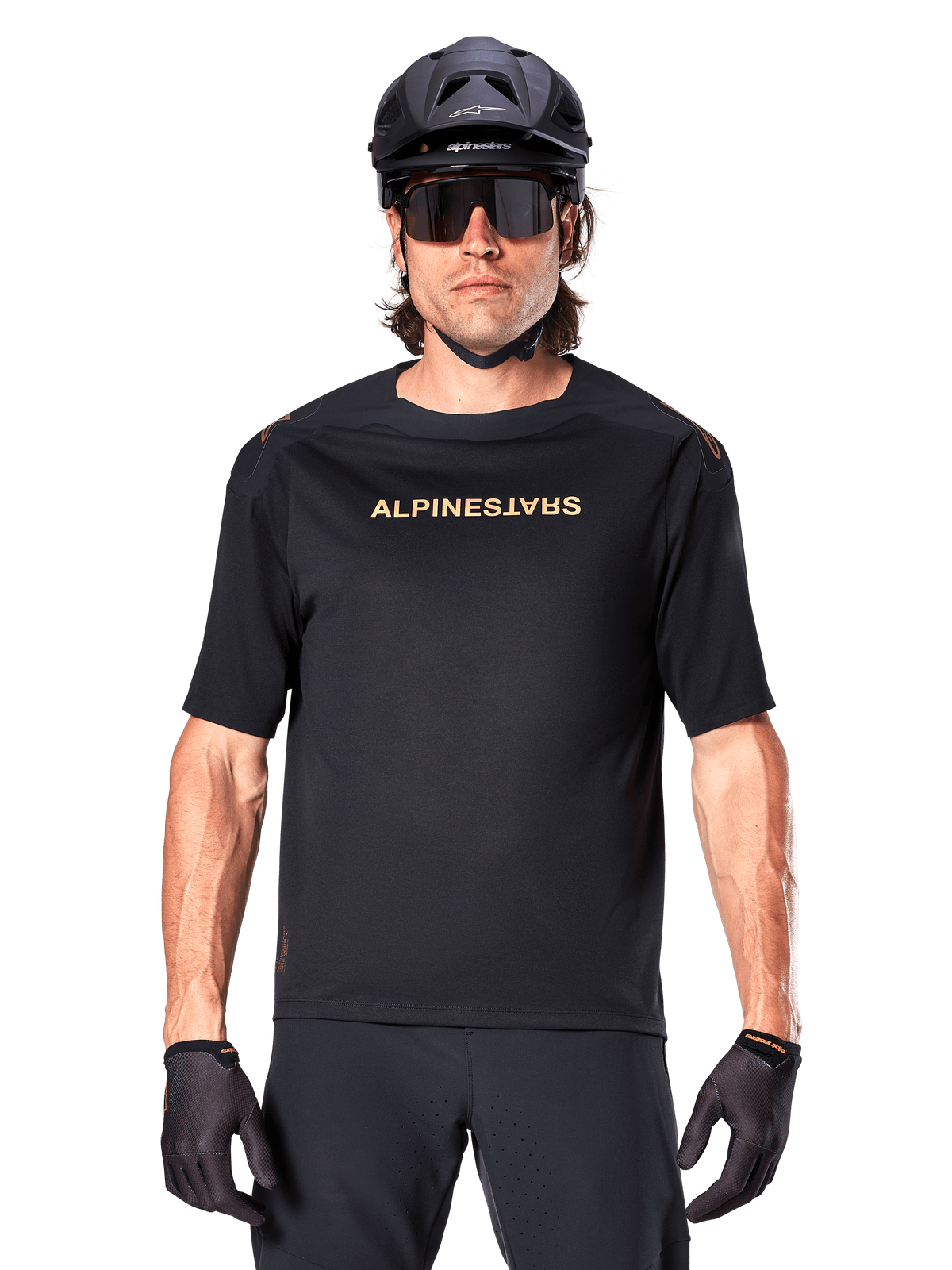 Ciclista de montanha com camisola Alpinestars A-Aria Polartec Switch de manga curta em preto, logótipo dourado no peito, capacete de BTT preto, óculos de sol de alta performance e luvas a condizer, equipamento de ciclismo para todo-o-terreno