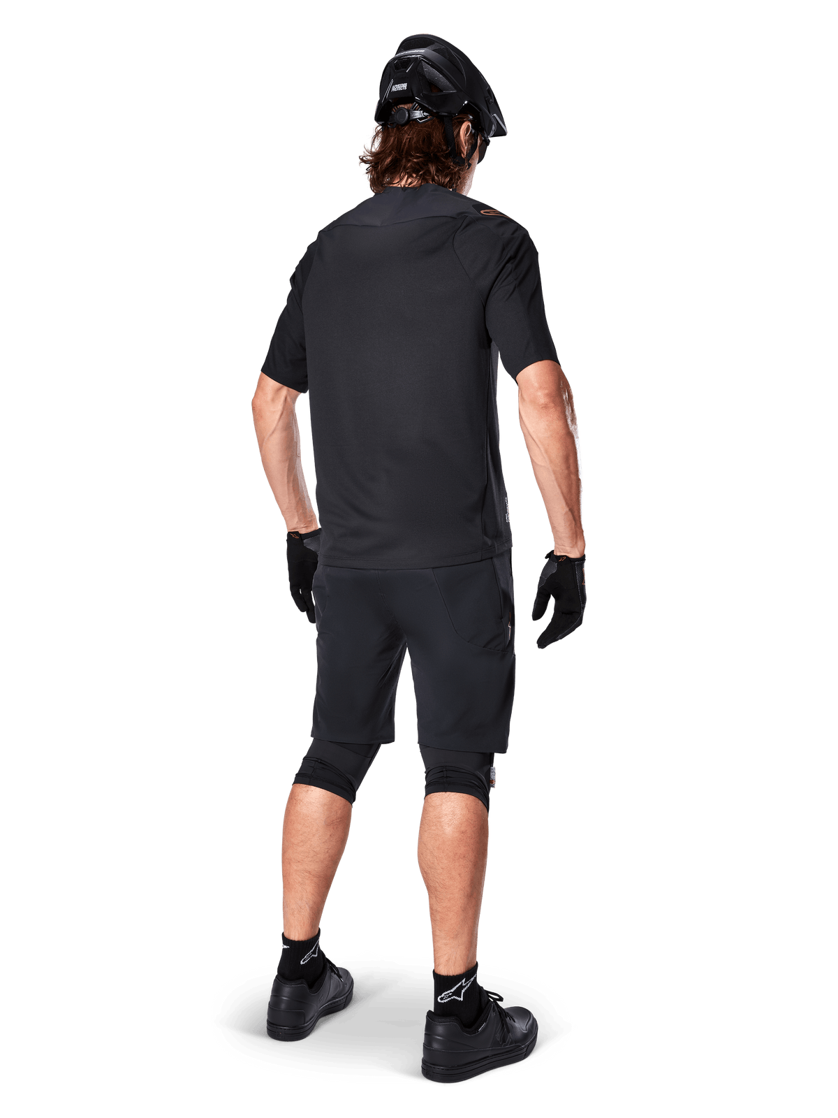 Ciclista de montanha masculino visto de costas com a camisola Alpinestars A-Aria Polartec Switch em preto, camisola de BTT de manga curta, combinada com calções de BTT pretos, capacete e luvas pretos, conjunto de performance coordenado para trilhos fora de estrada