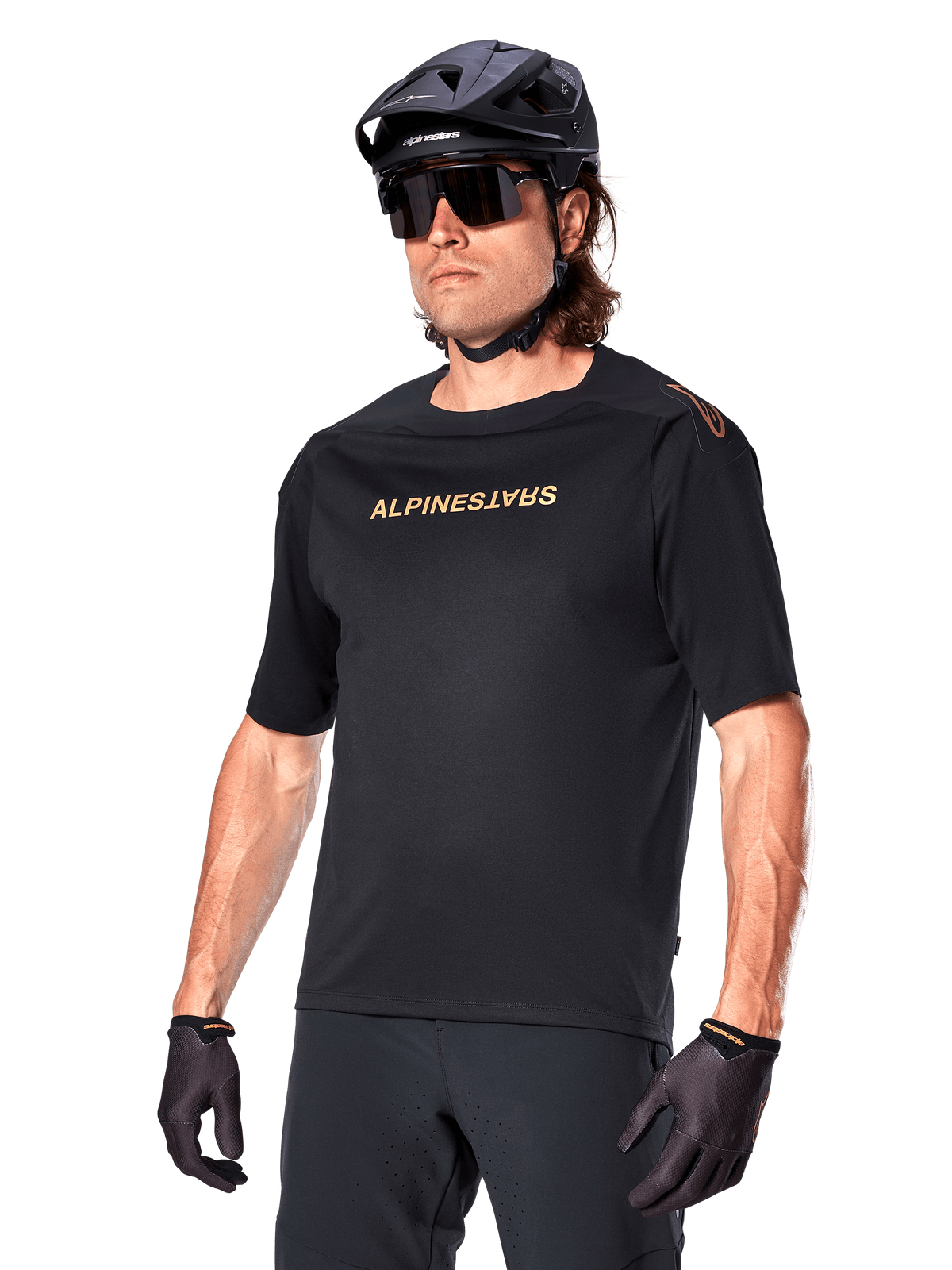 Alpinestars A-Aria Polartec Switch Jersey Short Sleeve, camisola de ciclismo de montanha preta com marca Alpinestars em dourado, usada com capacete, óculos de sol e luvas pretos, vestuário técnico de MTB