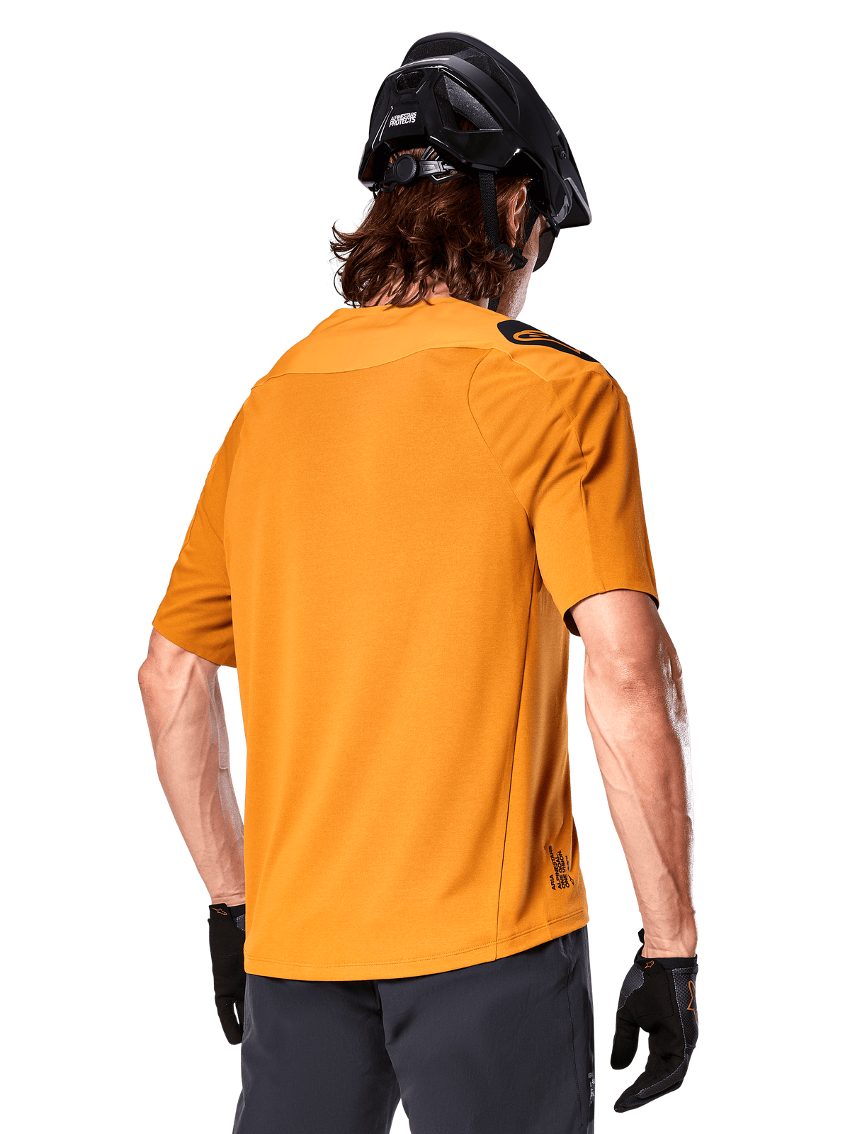 Camisola Alpinestars A-Aria Polartec Switch, camisola de MTB de manga curta, Dark Gold, vista traseira que mostra o ajuste de desempenho, usada com capacete preto e calções cinzentos, vestuário de trilhos durável e respirável