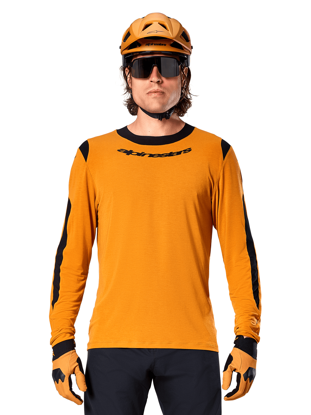 Modelo masculino a usar a camisola de manga comprida Alpinestars A-Dura Dri Wool em Dark Gold, coordenada com um capacete de BTT e luvas em dourado a condizer, painéis de malha pretos nos ombros e mangas, logótipo Alpinestars preto no peito, óculos de sol e calças escuras, vestuário técnico de BTT