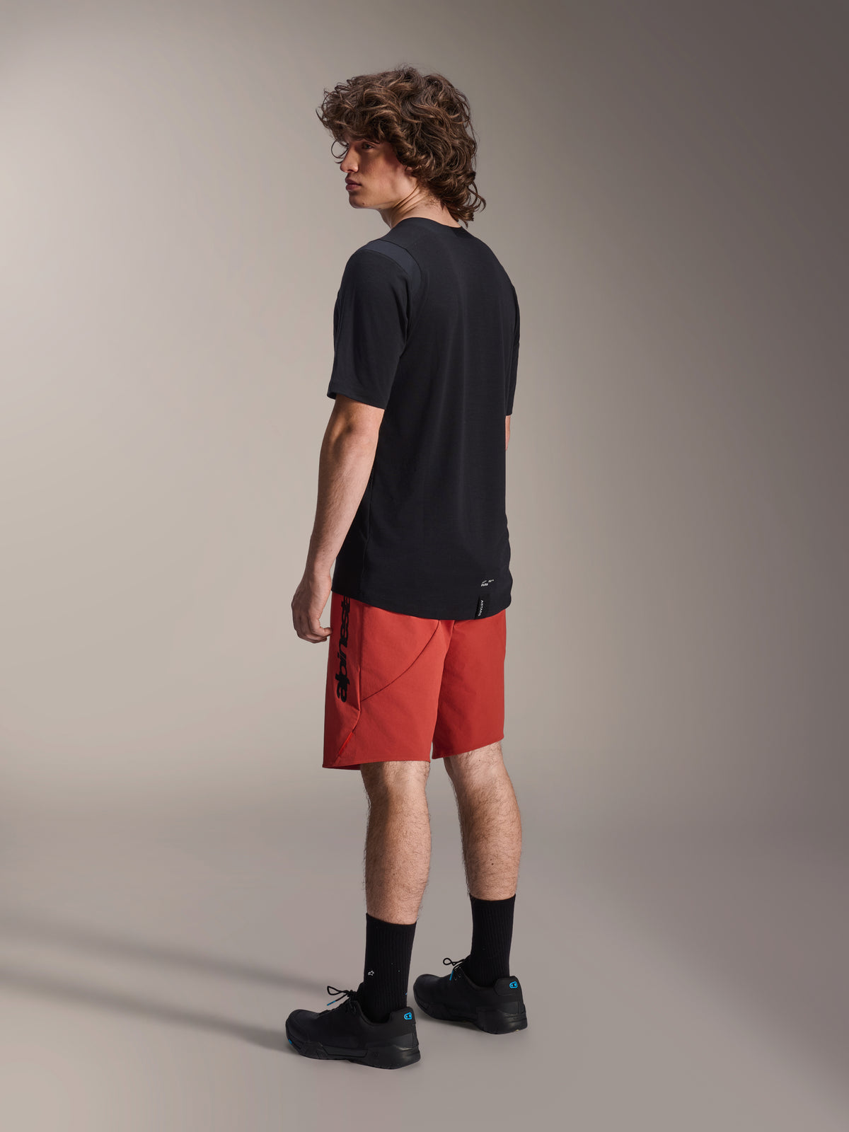 Alpinestars A-Dura Elite Shorts, Mountain Bike Shorts, Dark Orange, worn with a black short-sleeve jersey and black mountain bike shoes, rear side view of model highlighting performance fit and branding