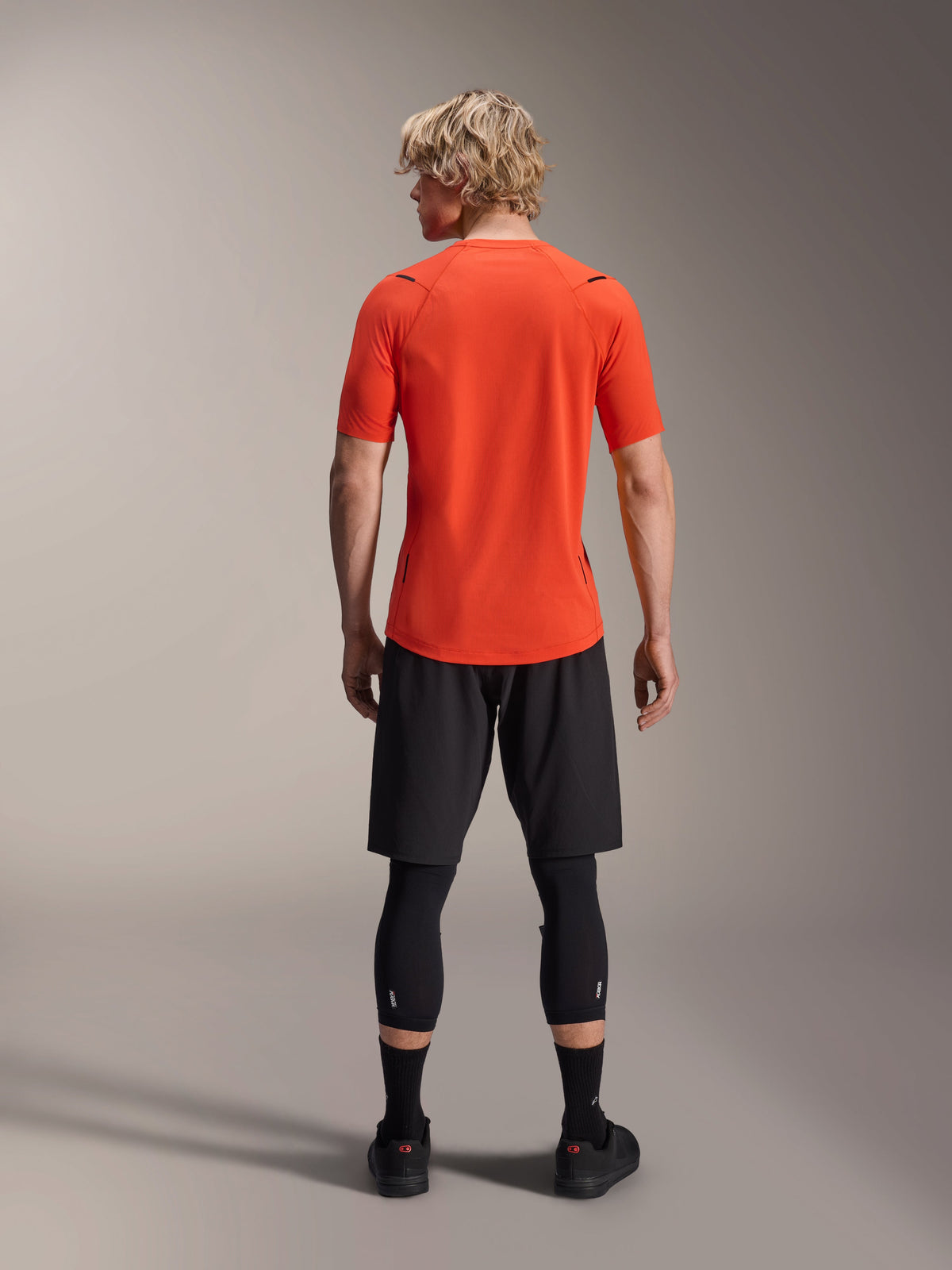 Camisola Alpinestars A-Aria Astar, camisola de BTT de manga curta, Spicy Orange, vista traseira mostrando o corte de desempenho e a cauda alongada, combinada com calções de ciclismo pretos e leggings